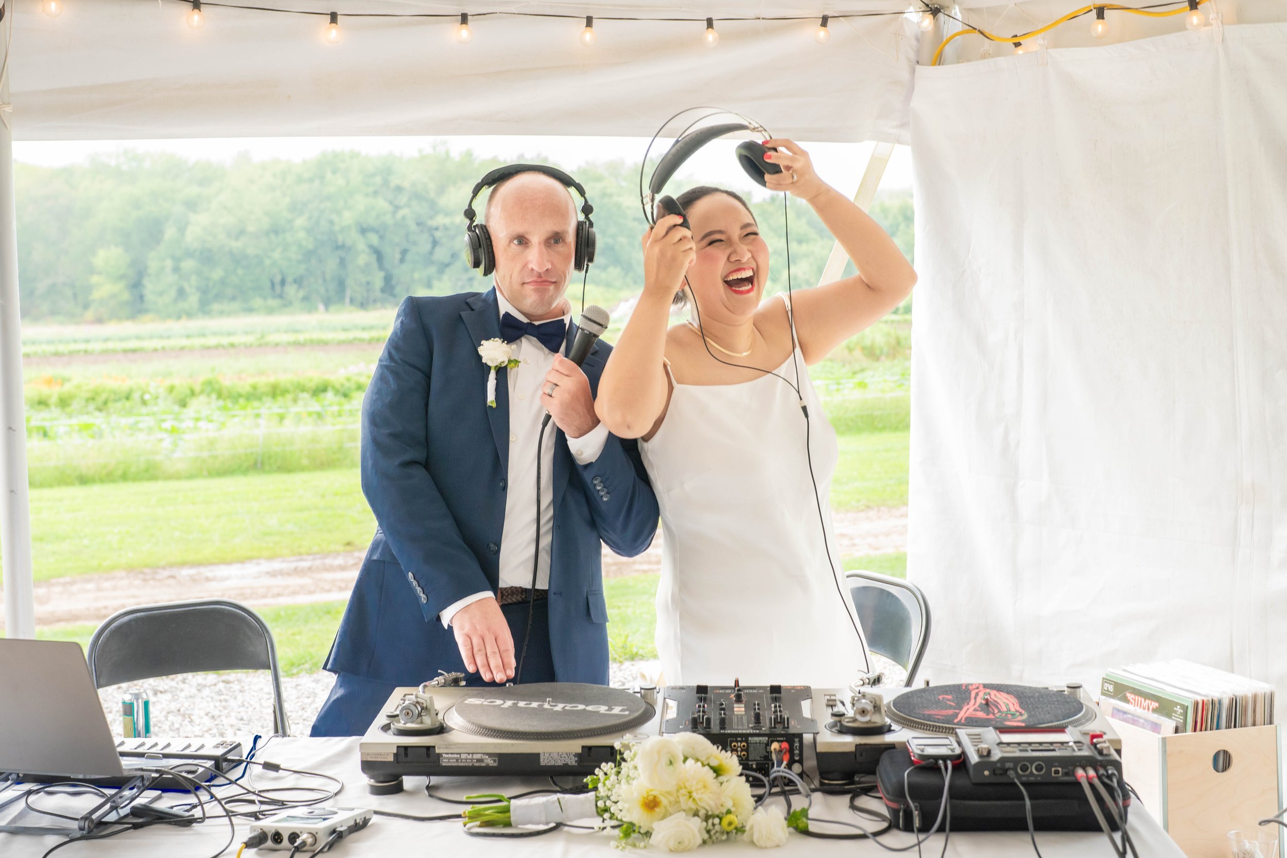 A bride and groom, dressed in wedding attire, are enjoying a moment as a DJ performs at their outdoor wedding reception.