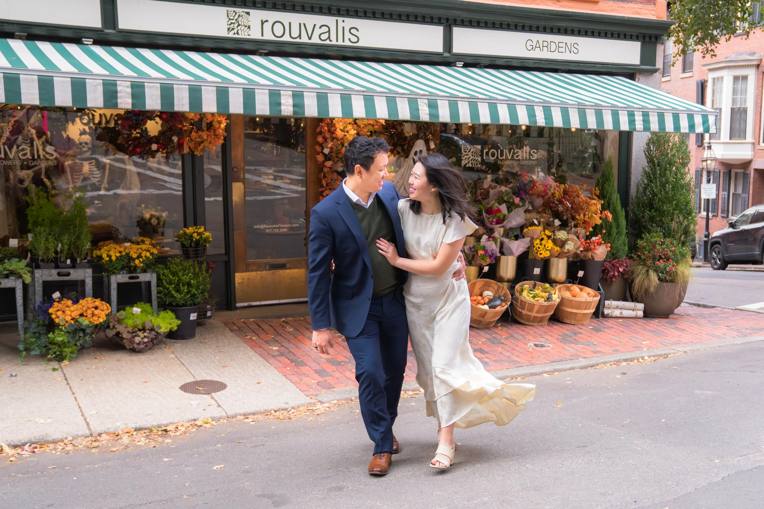 A couple dressed in wedding attire walking hand in hand outside a flower shop, celebrating their wedding day.