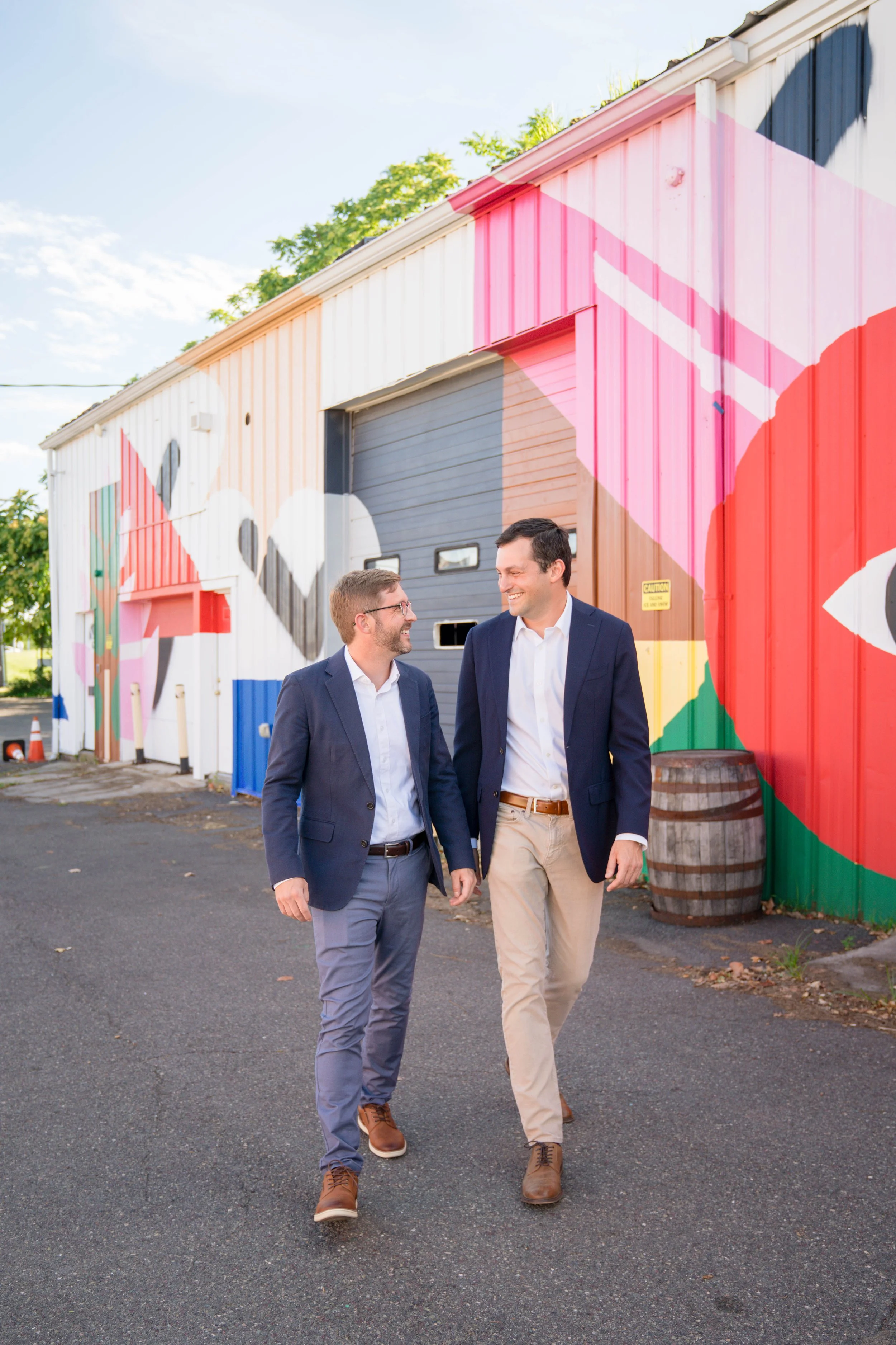 Two men in suits walking and talking outside in front of a colorful mural on a building