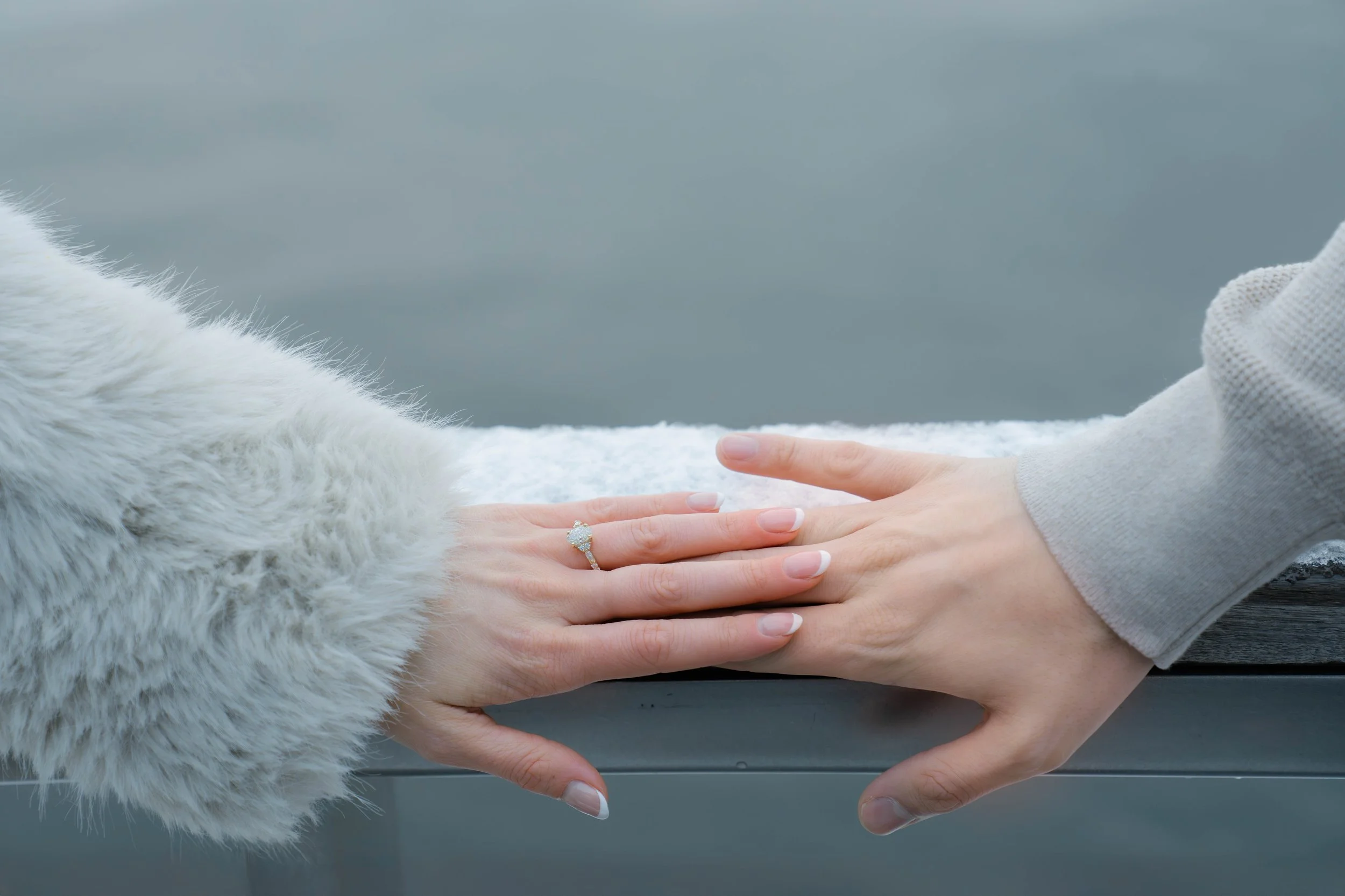 Close-up of hands with a wedding ring against a gray background.
