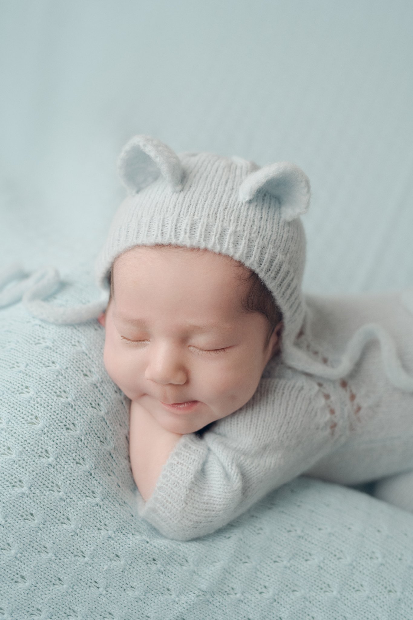 Retrato newborn con bebé dormido sobre manta blanca y gorrito tejido artesanal. Fotografía profesional Yamipic