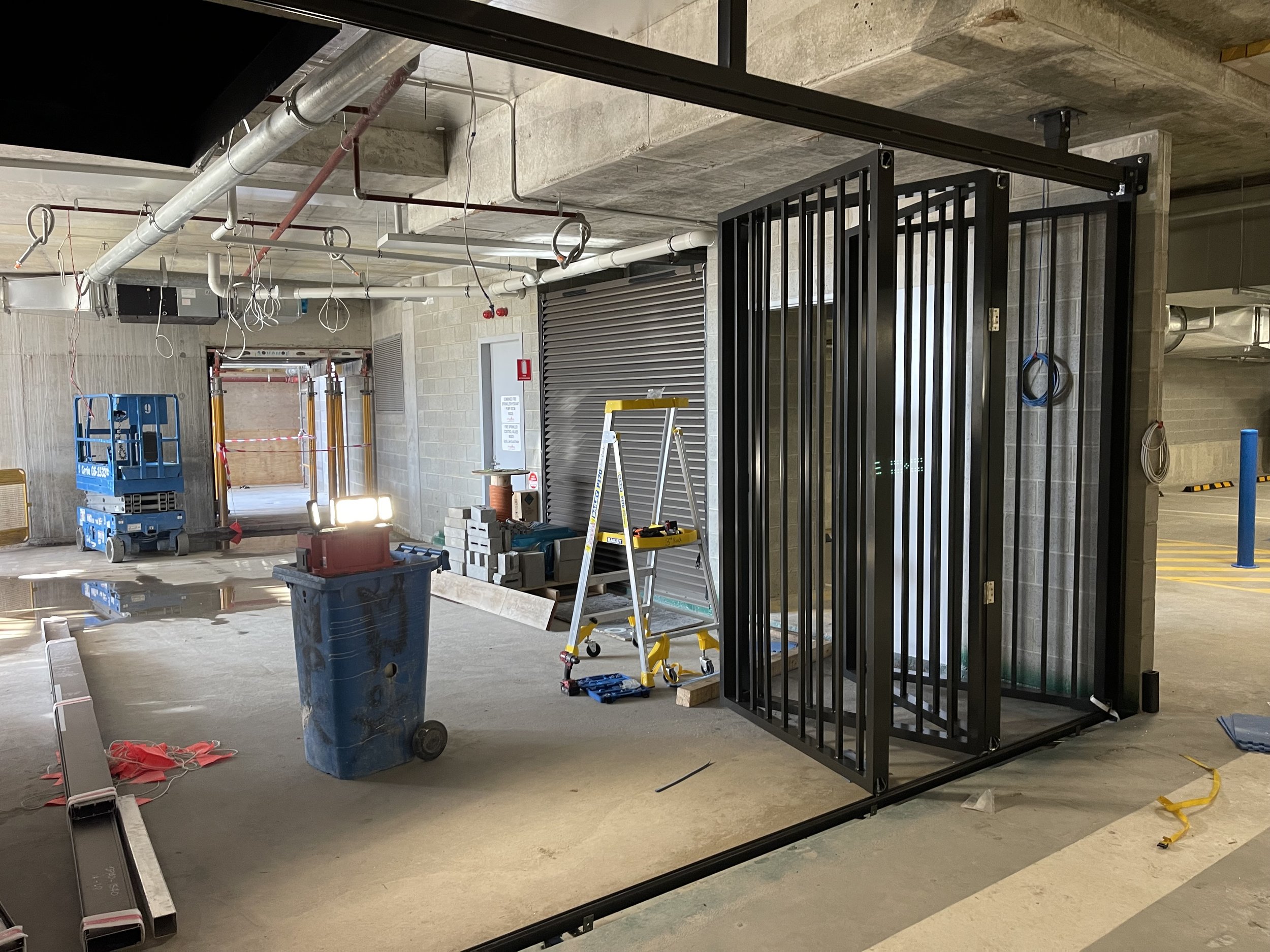 Construction site in an underground parking garage with safety barriers, tools, a ladder, and a black metal cage.