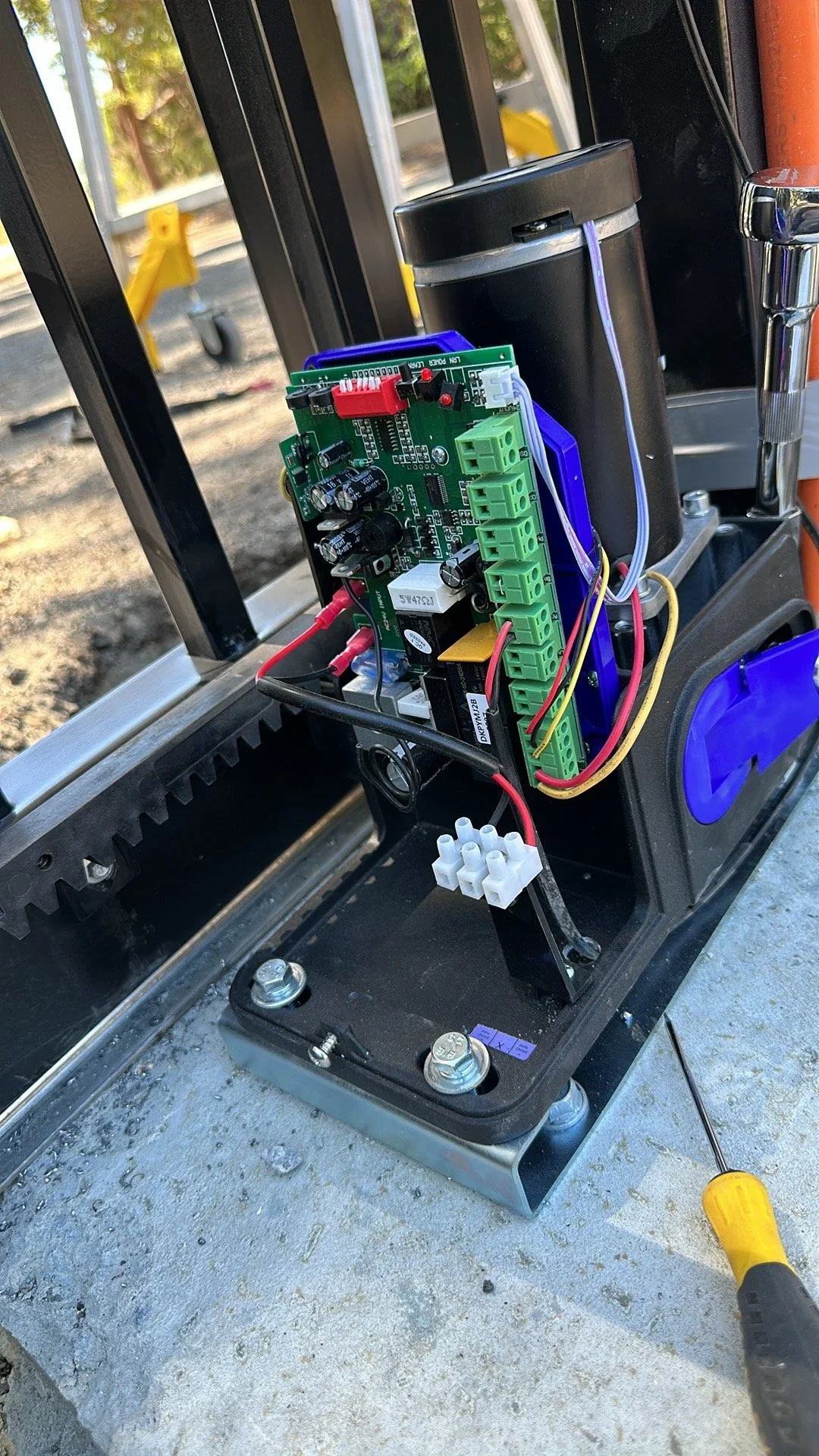 Close-up view of an electronic circuit board with wiring installed on a mechanical structure, with tools nearby, outdoors.