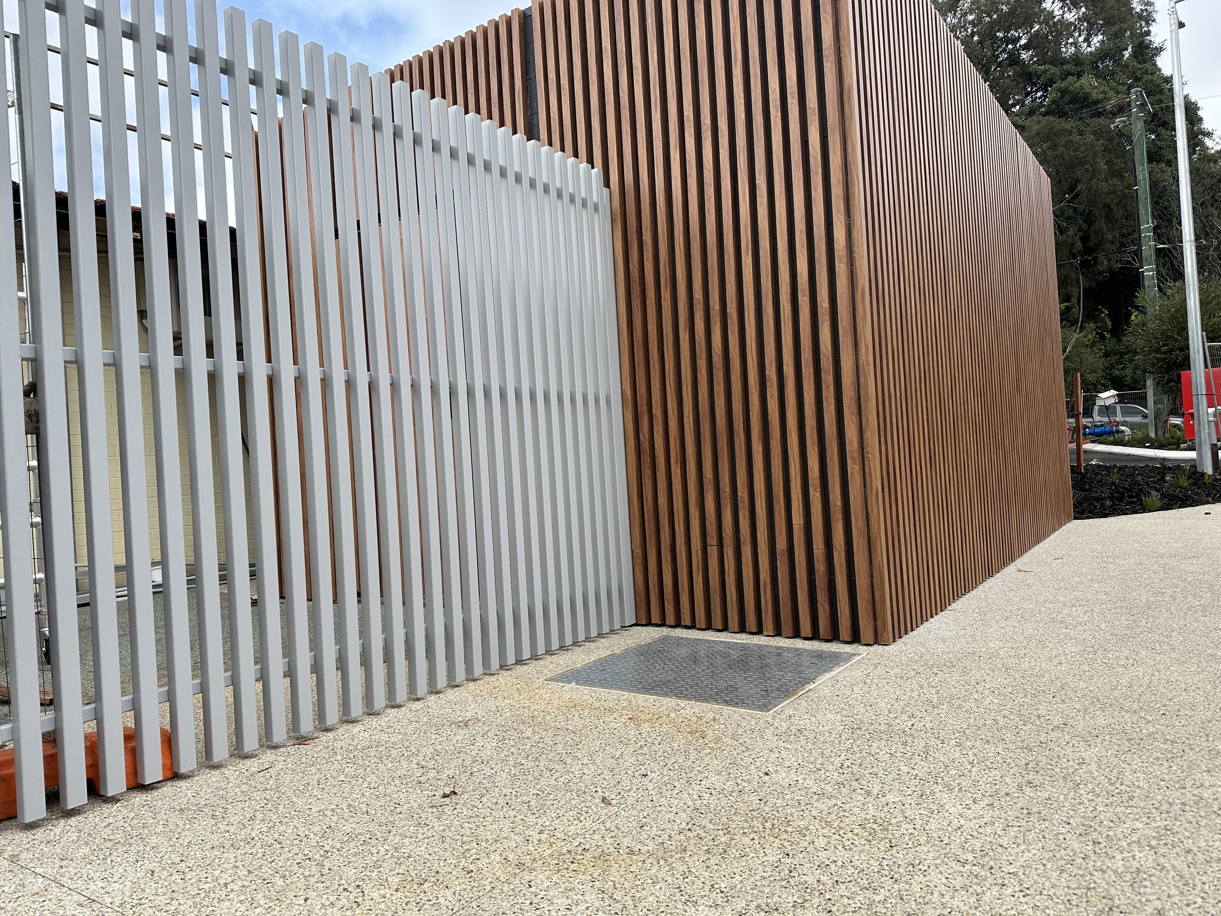 Modern building exterior with vertical wooden slats and a metal fence on concrete ground.