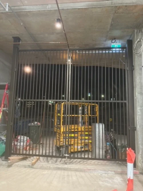 Steel security gate installed in an indoor parking area with construction tools and equipment nearby.