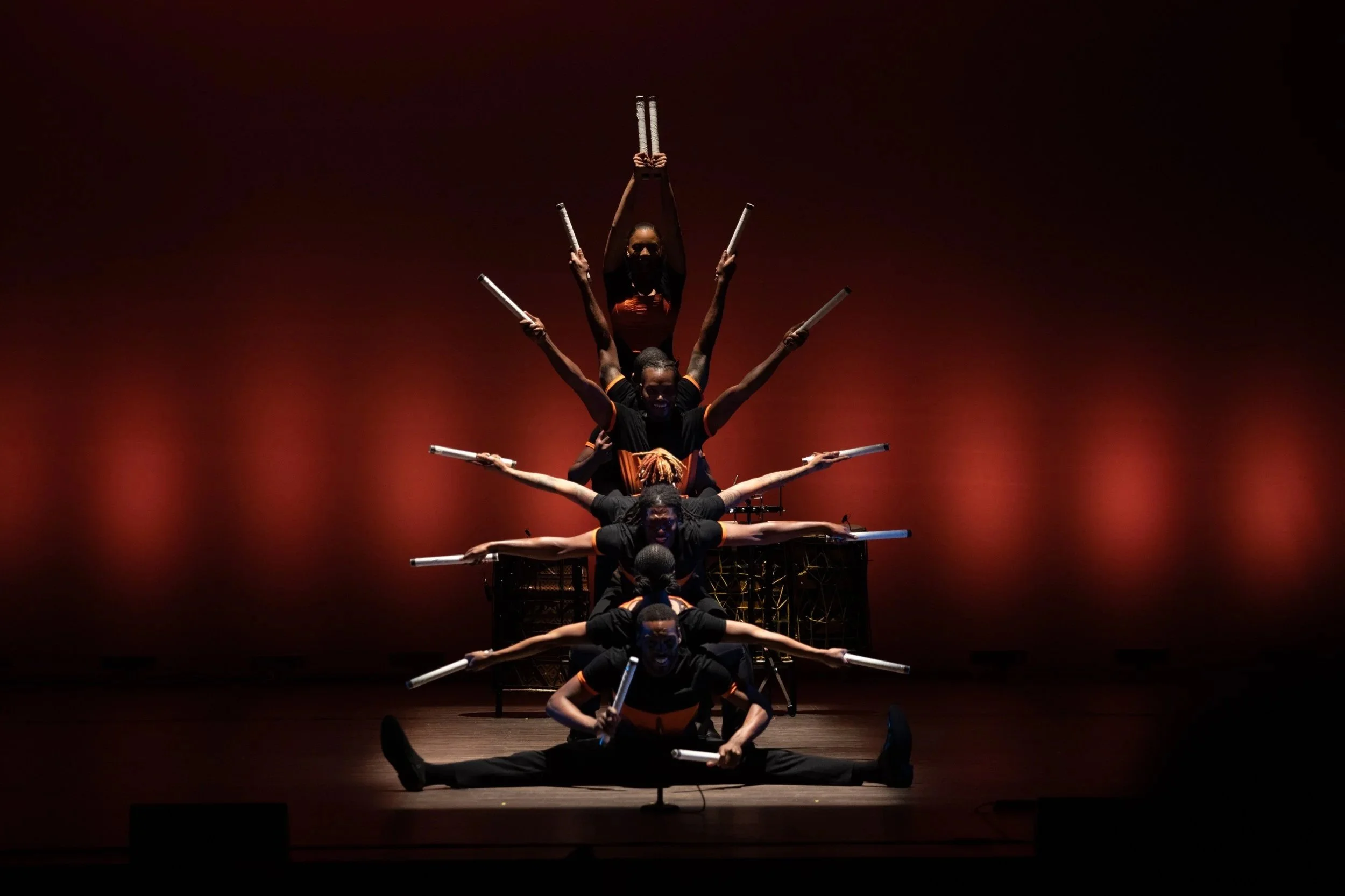 A group of six performers stacked vertically on stage, creating a balanced pyramid formation at the Marcus Center for Performing Arts in Milwaukee. 