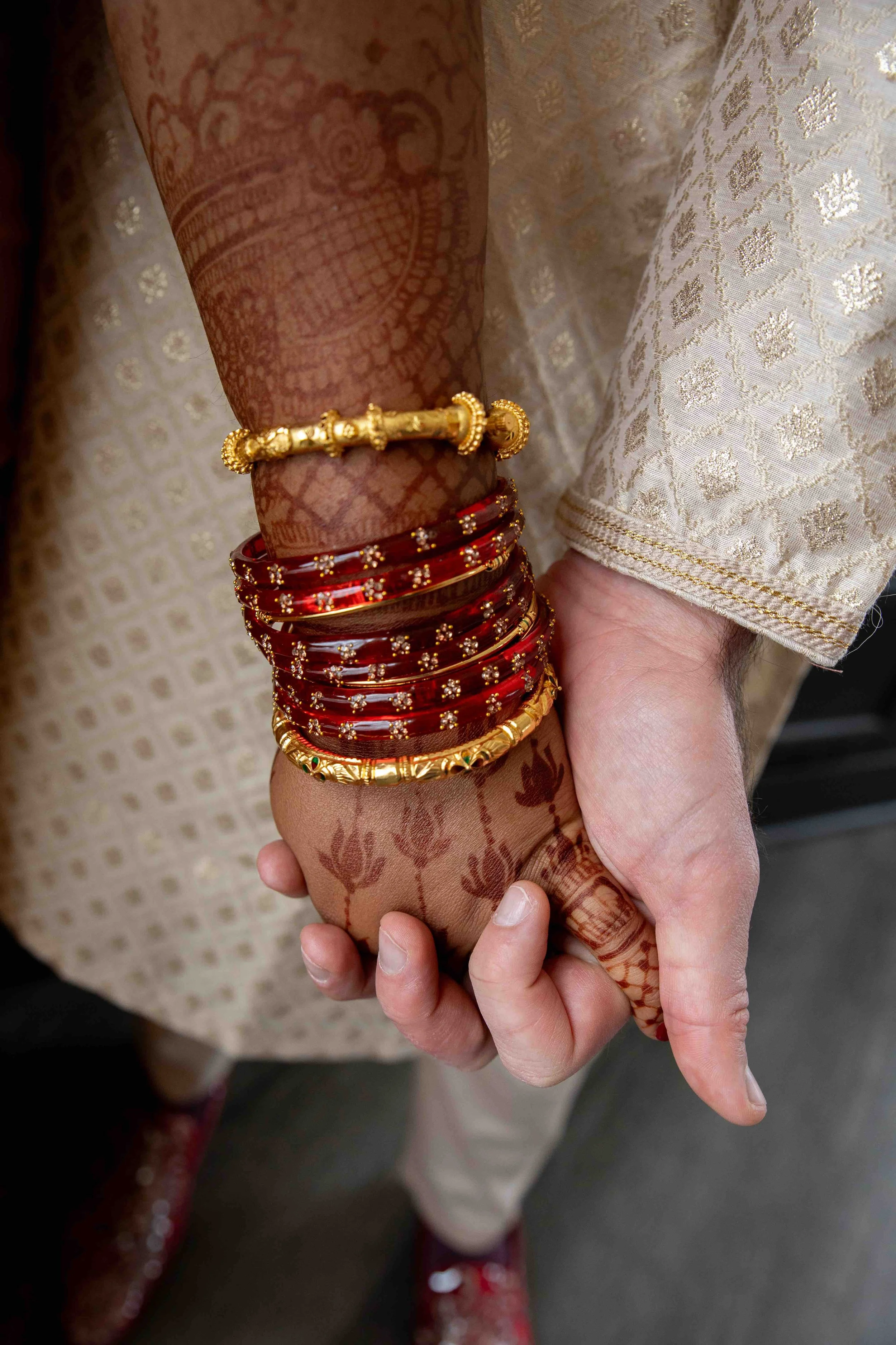 A person with traditional Indian bridal jewelry and mehndi hand henna art, wearing a white garment with intricate gold embroidery.