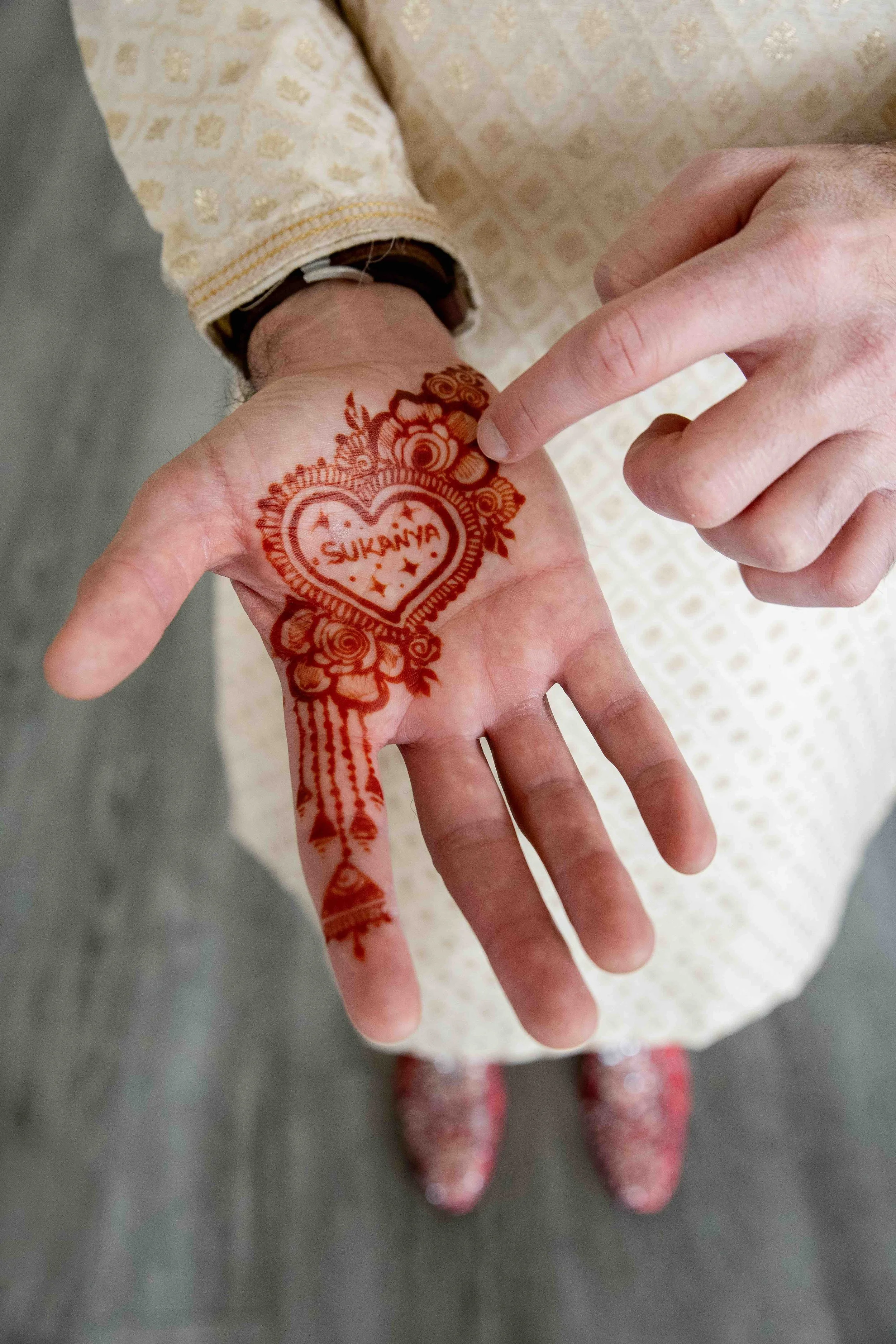 A person with a henna tattoo on their hand that says 'Sukanya' inside a heart, surrounded by floral designs.