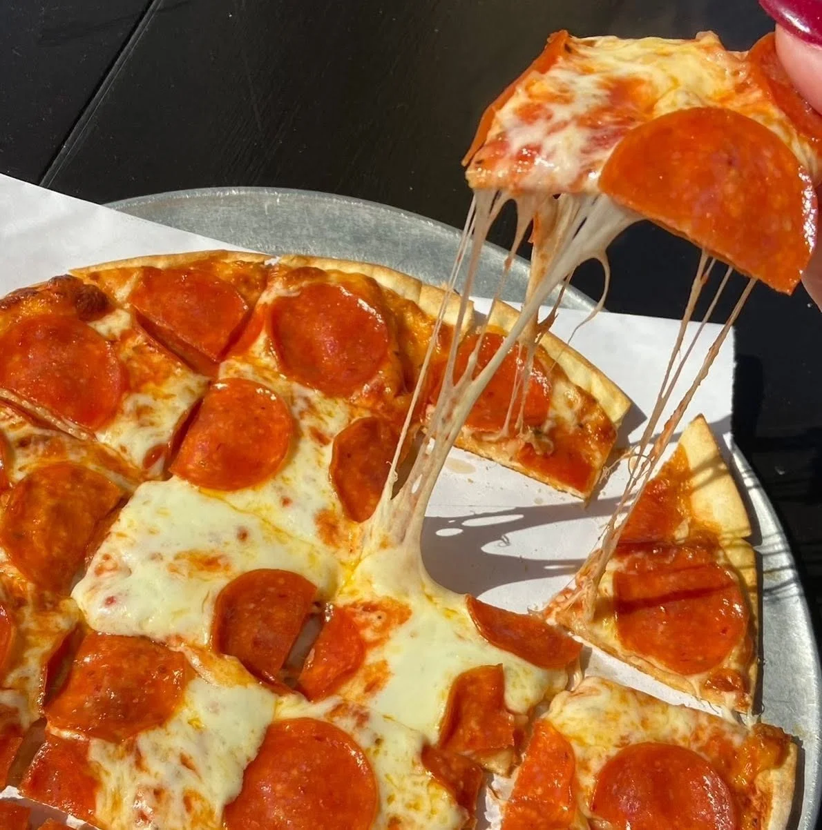 Close-up of a pepperoni pizza with melted cheese stretching as a slice is being lifted.
