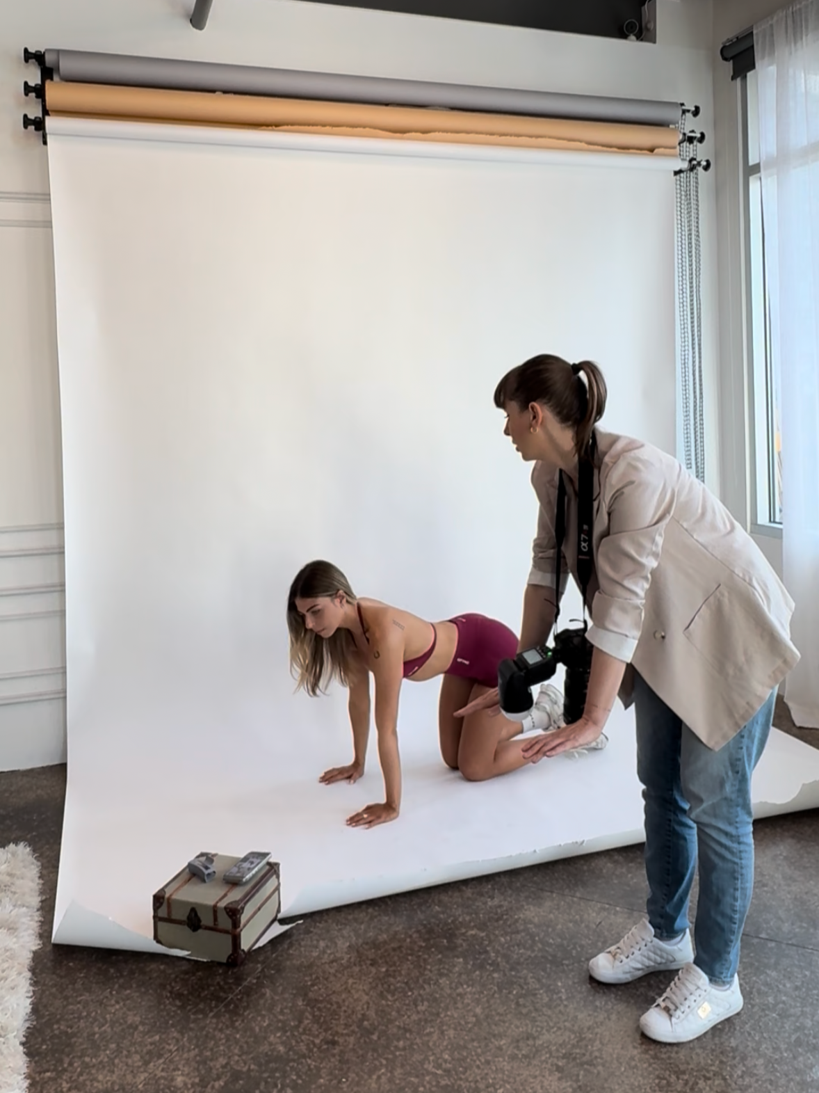 Mosel Coach and Photographer is showing poses to a woman in sportswear on a white backdrop in a studio.