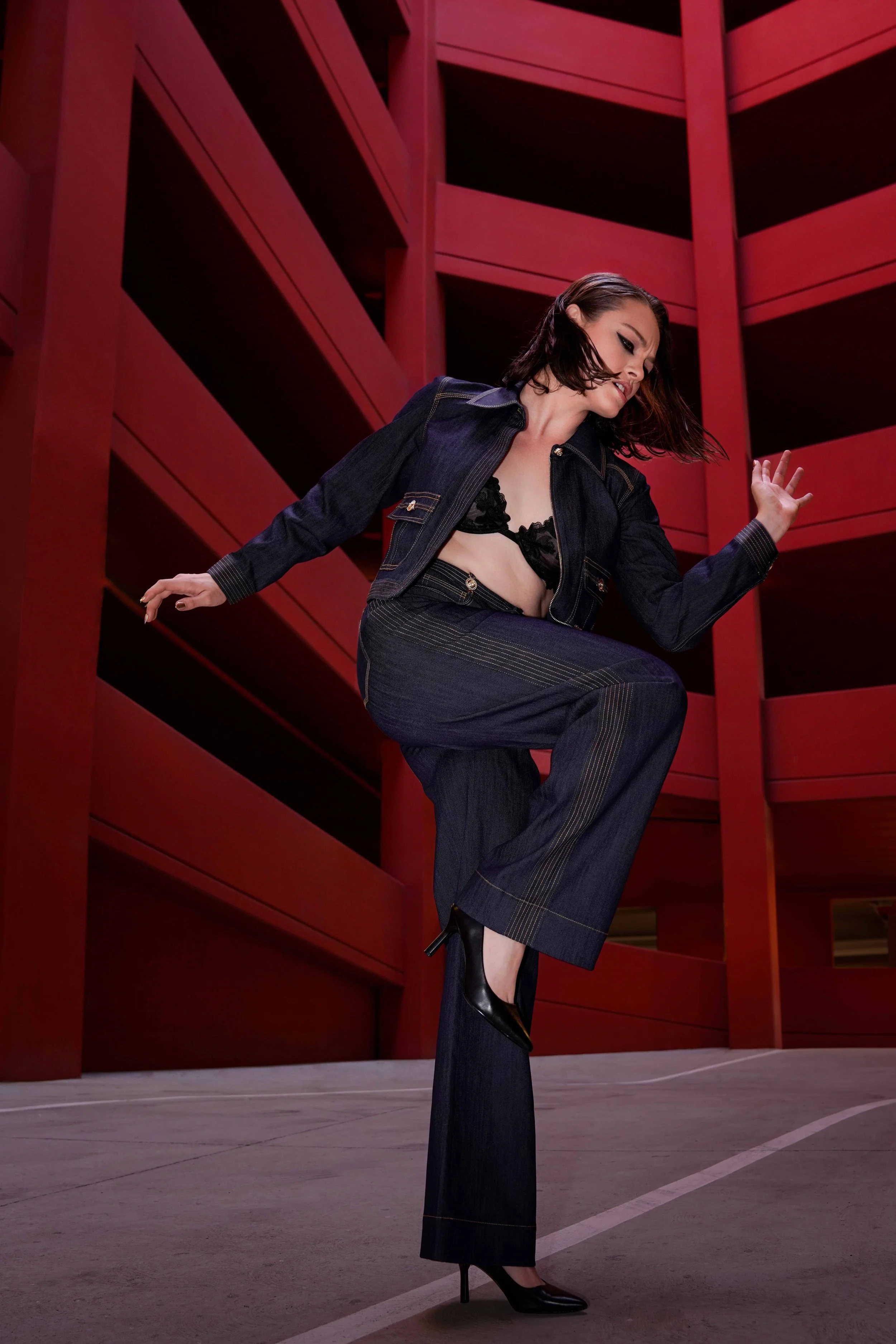high fashion photoshoot - female model with brown hair is posing in a red garage setting with a denim set.