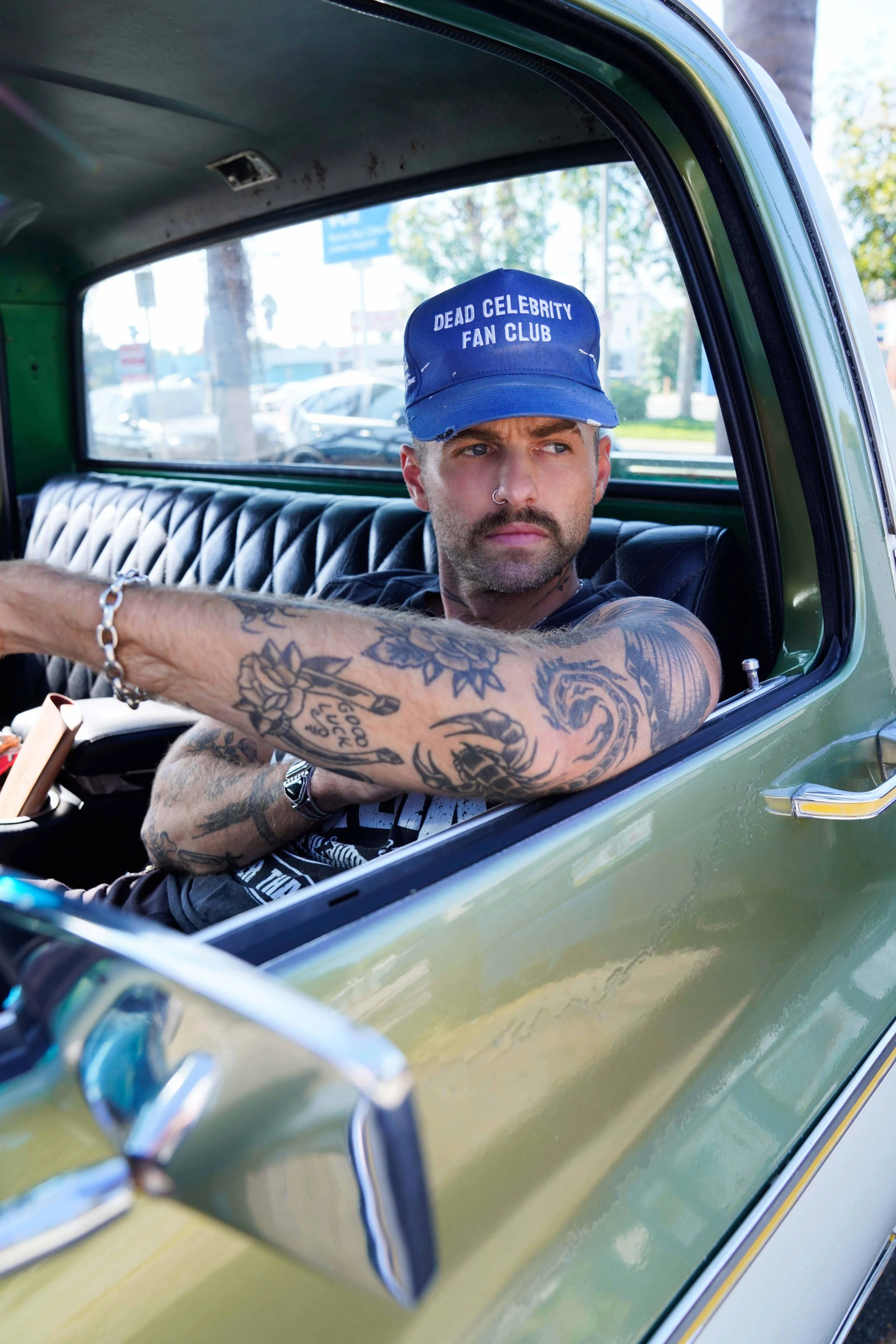 Male model with tattoos in Los Angeles is sitting in his truck and wearing a hat.