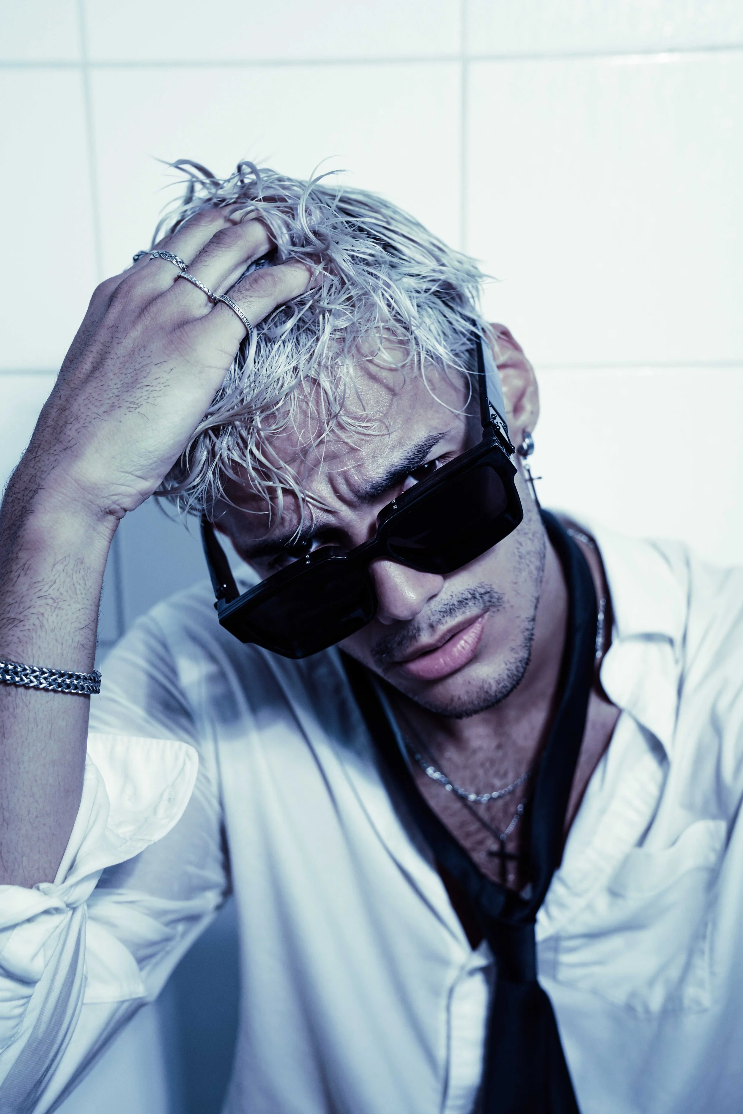 Blonde male model is posing in a bathtub, wearing a white button-down shirt with a black tie and black sunglass. 