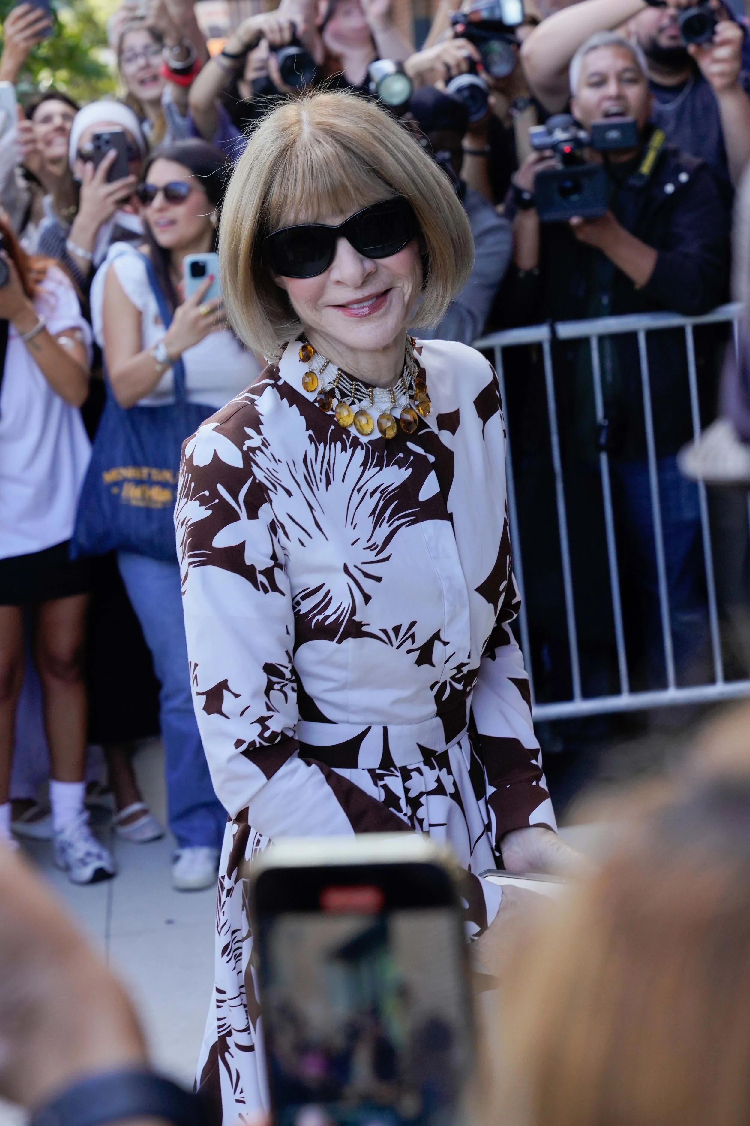 Anna Wintour at Michael Kors SS26 fashion show in NYC wearing black sunglasses and a flower dress.