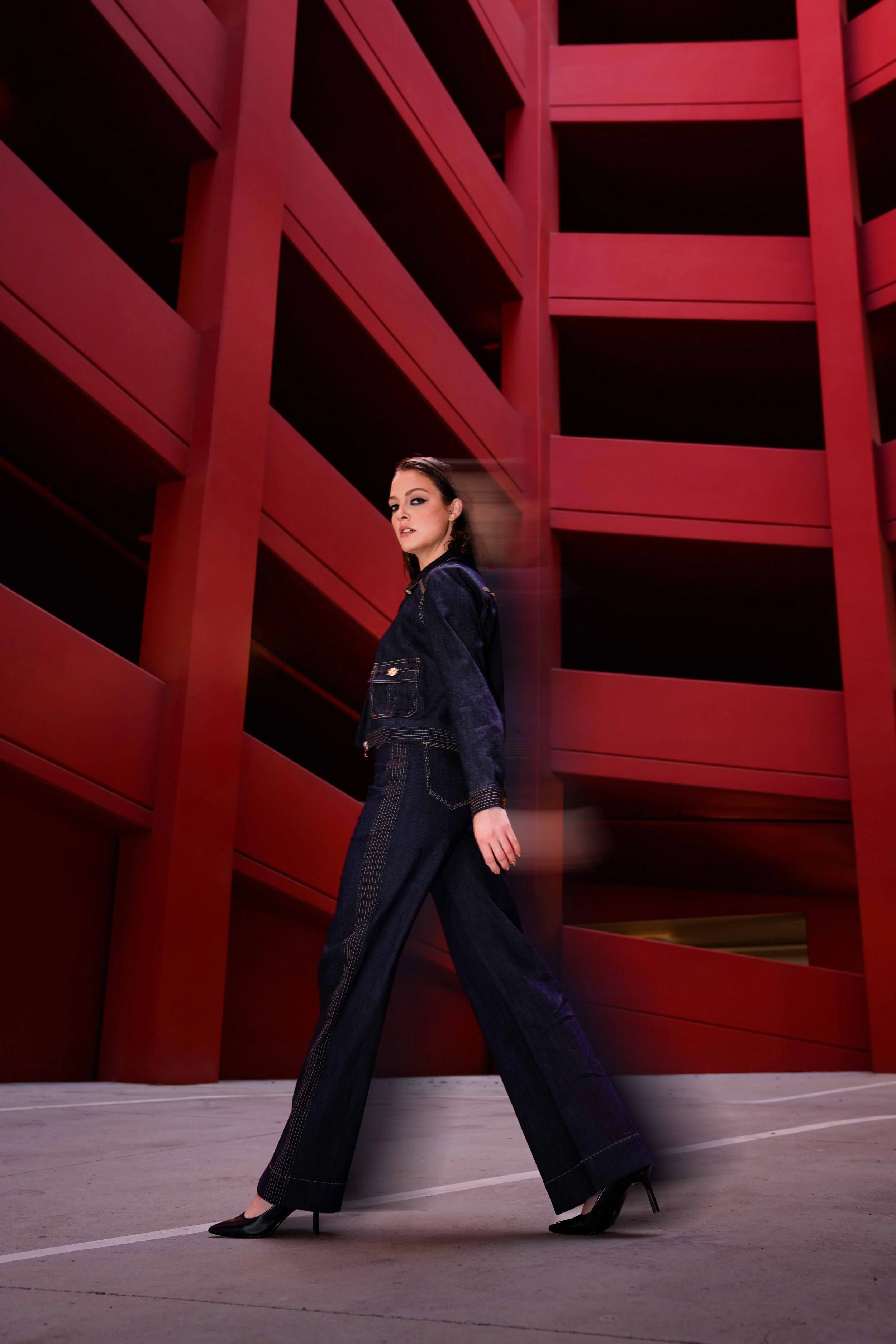 high fashion photoshoot - female model with brown hair is posing in a red garage setting with a denim set.
