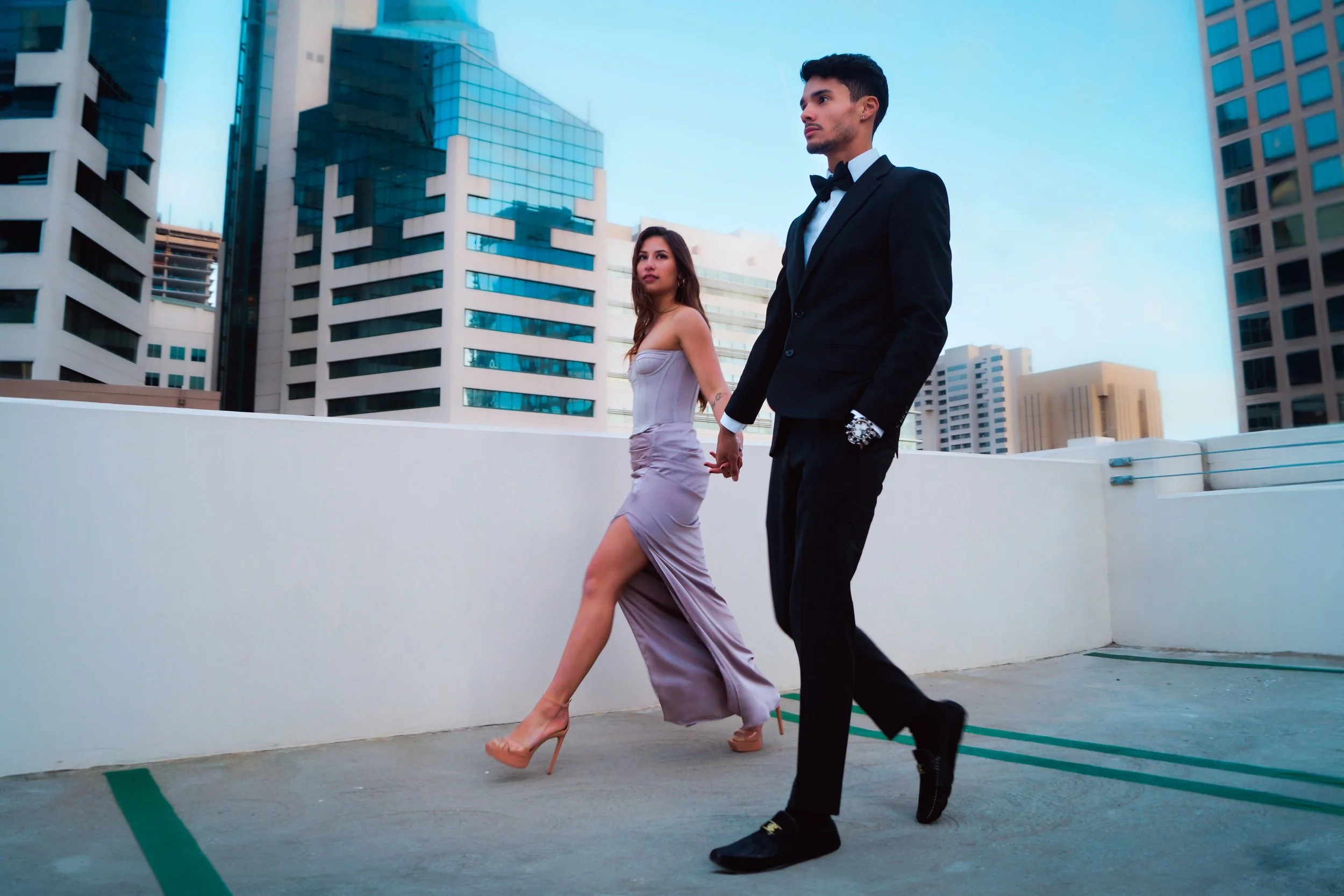 Female and male couple in elegant evening outfits walking hand in hand on a roof top in San Diego.