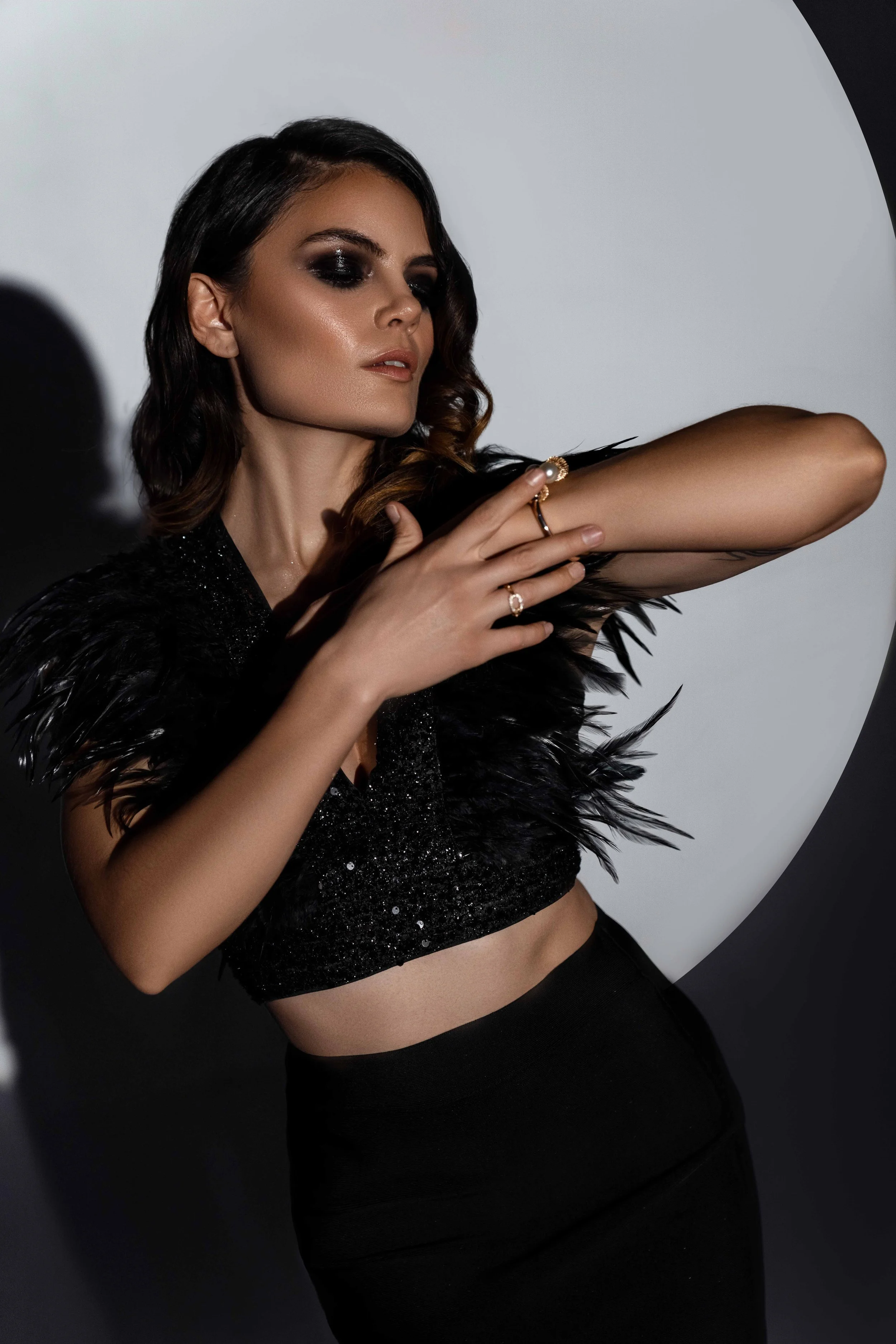 Female model is posing in an elegant outfit with feathers in a photo studio, in front of a spotlight.