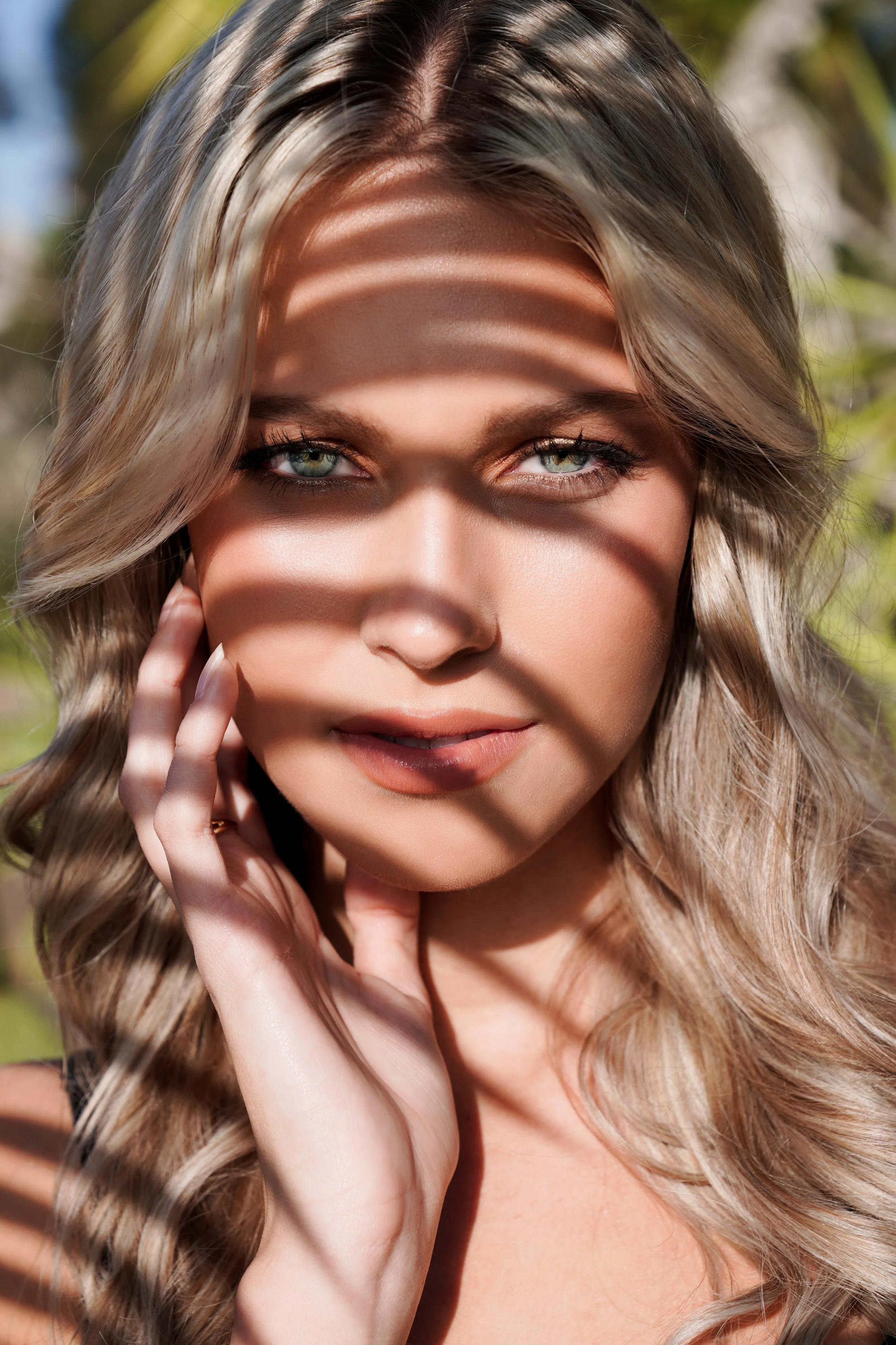 Close-up editorial beauty portrait featuring a blonde female model with glowing natural skin and dramatic shadow play across her face. Captured with creative lighting, this high fashion beauty photography highlights flawless skin texture, soft makeup