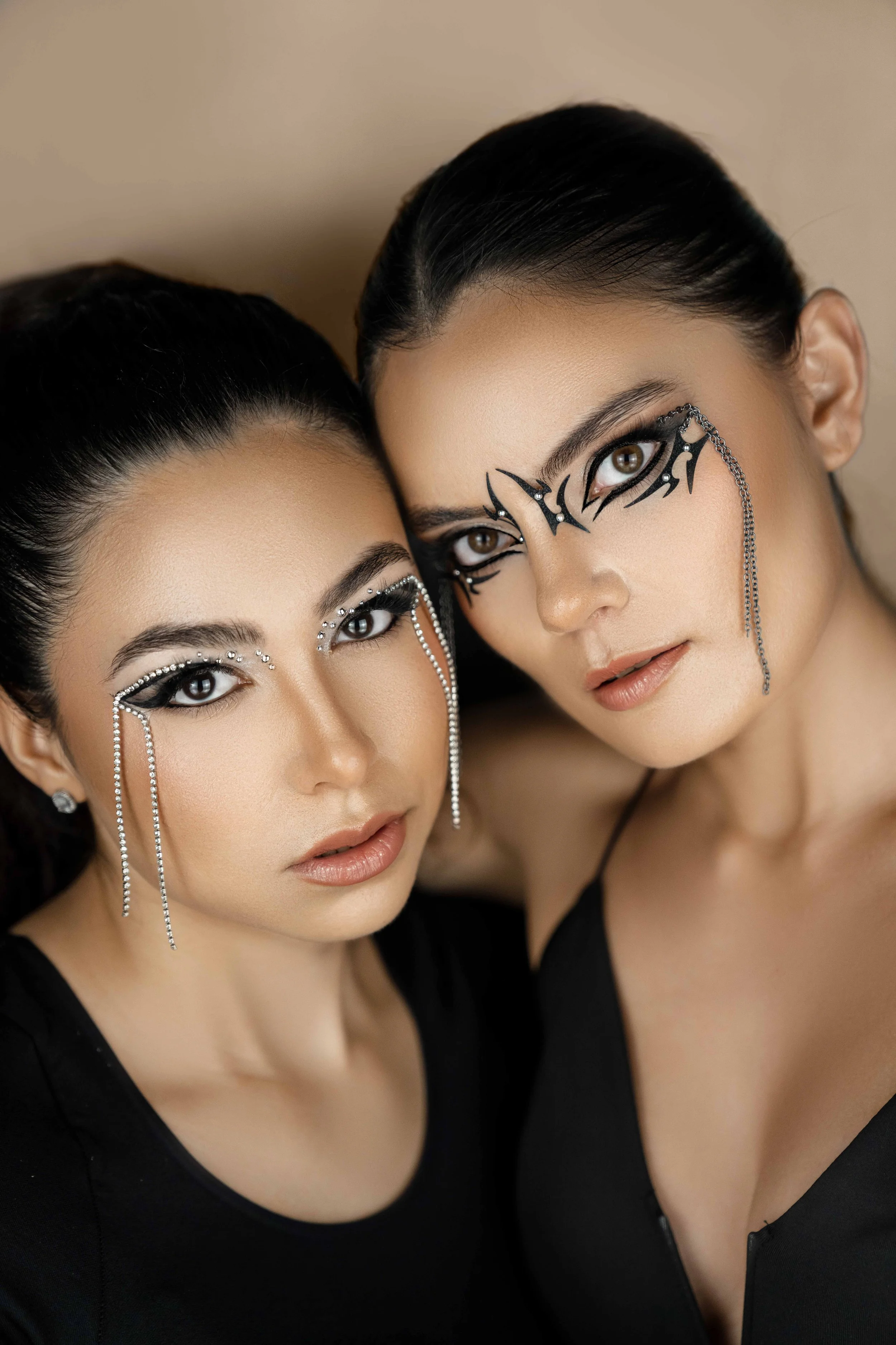 2 Female models are posing at a beauty photoshoot in a photo studio. They are wearing an edgy makeup and black shirts.