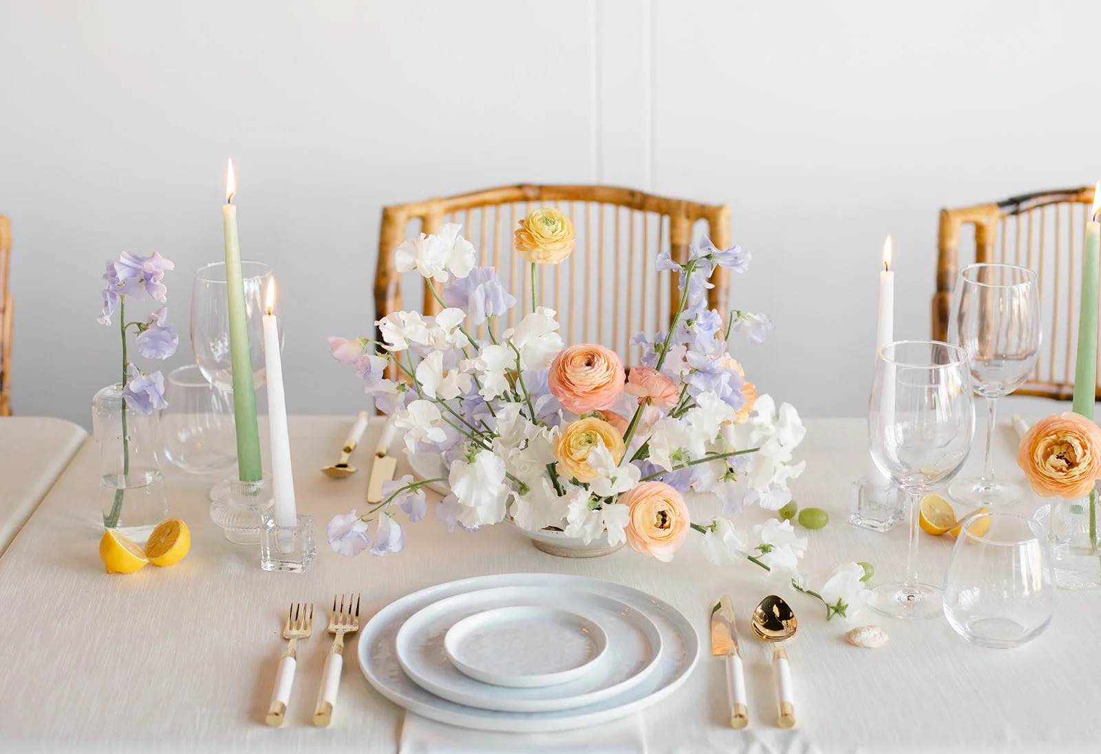 A table setting with a floral centerpiece, candles, dishes, glasses, and cutlery, decorated with lemon slices and small shells.