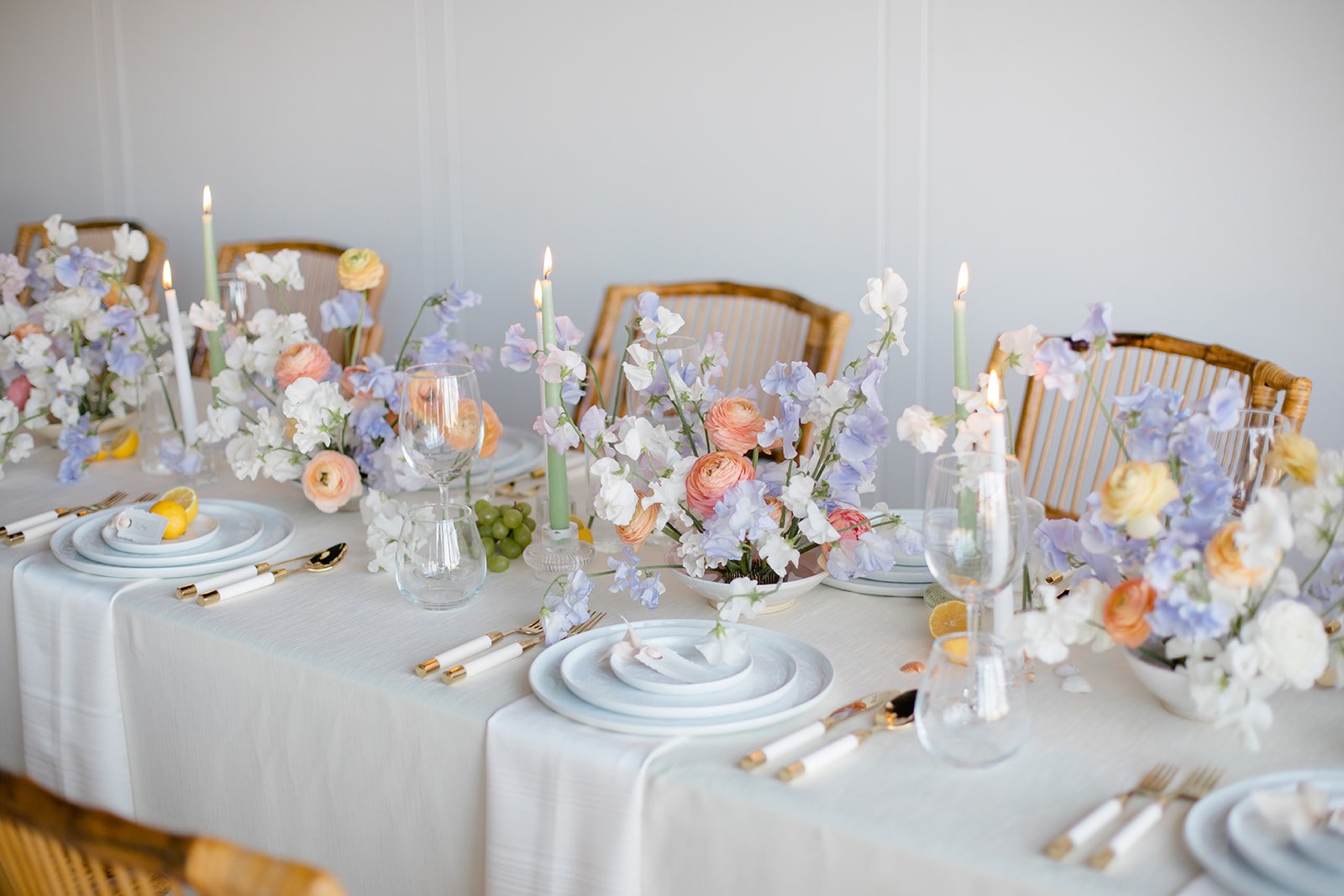 Elegant dining table decorated with pastel-colored flowers, white candles, wine glasses, and gold-accented cutlery, set for a formal event.