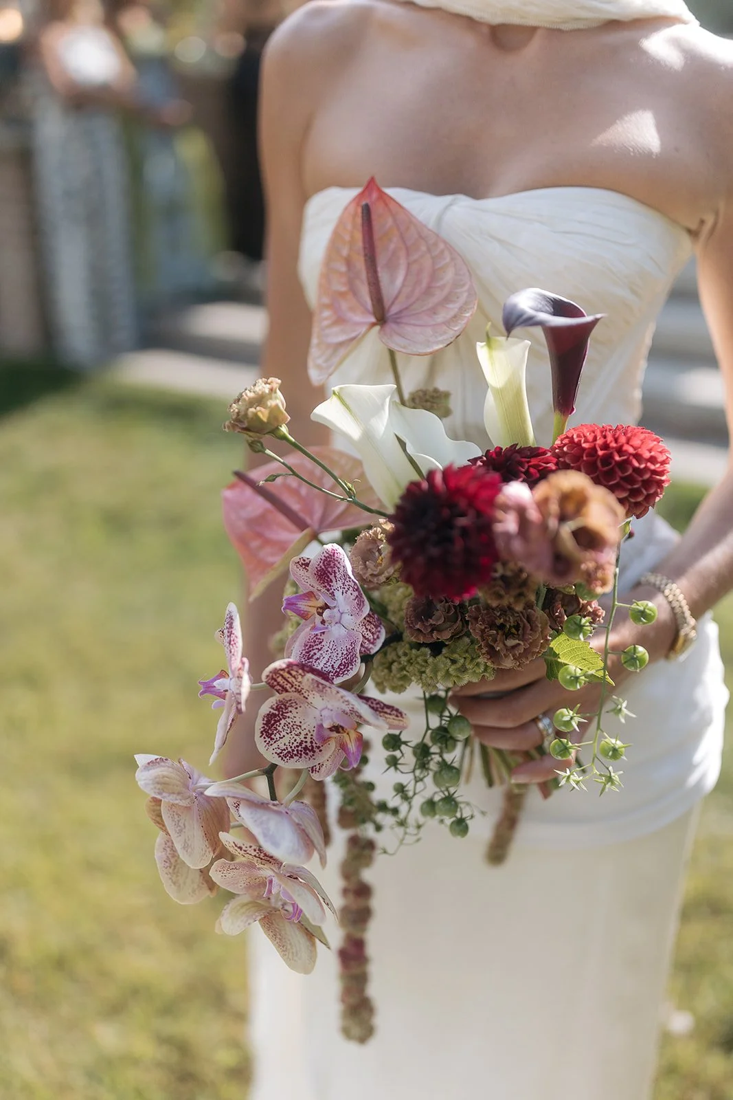 A modern bride in a strapless white dress holding a bouquet of modern, simple, artful flowers.