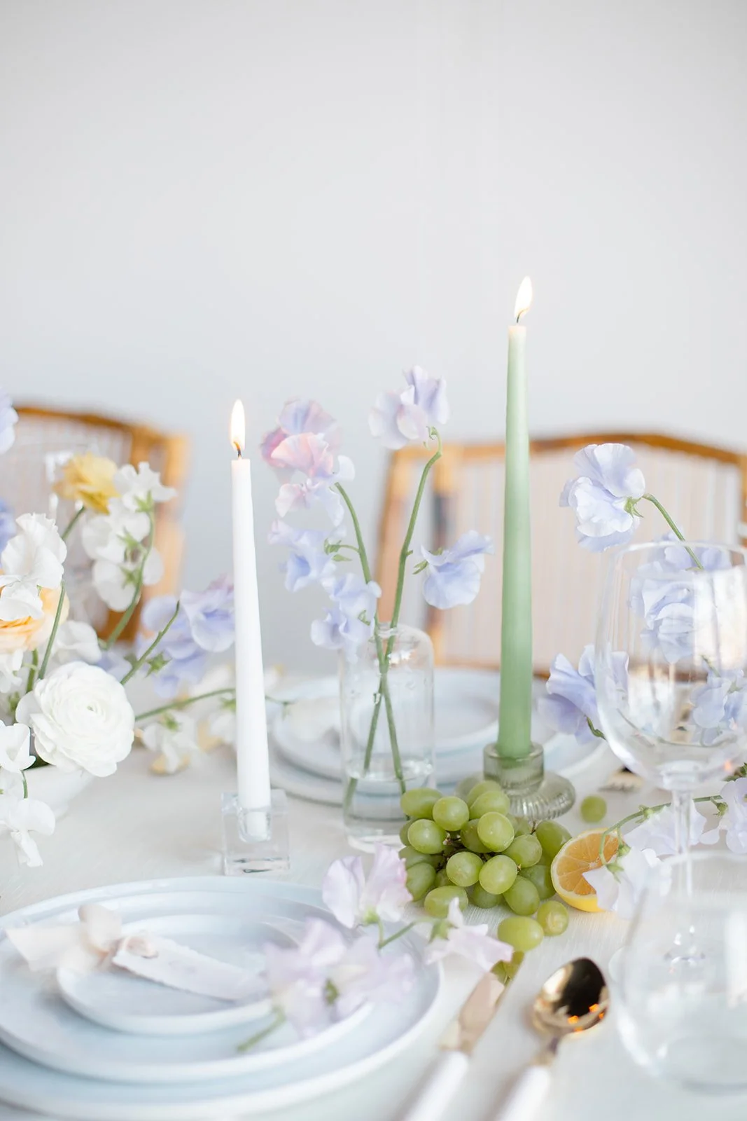 Elegant table centerpiece with pastel flowers, green candles, grapes, lemon slices, and elegant tableware.