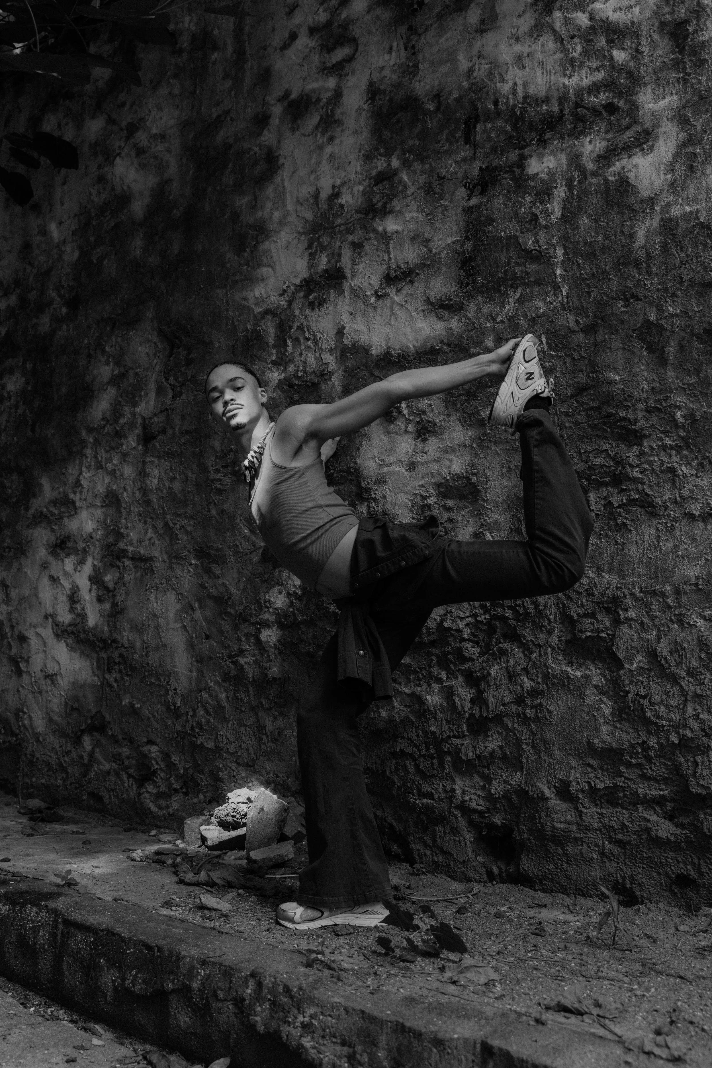 A person performing a yoga pose against a textured wall, wearing casual clothes, in black and white.