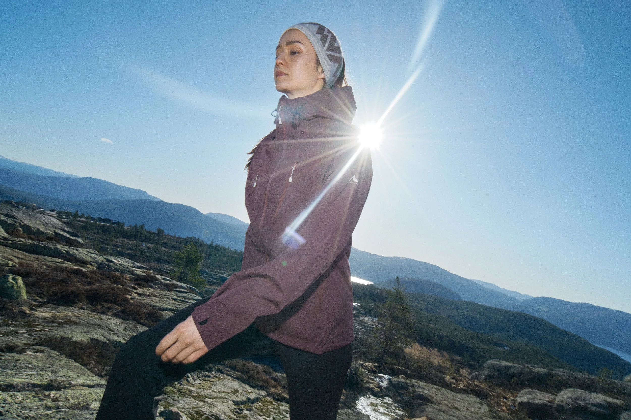 Model in a McKINLEY outdoor jacket on a rocky ridge in backlit sunlight for the FW26 collection campaign