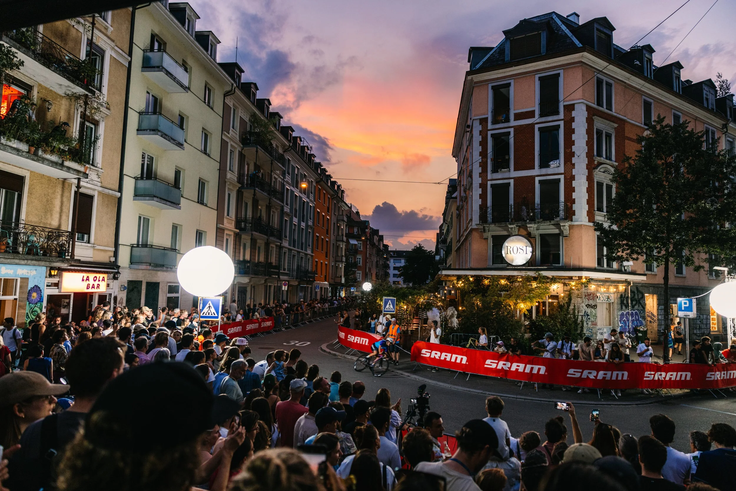 Cyclists racing through Zurich city centre at dusk during ZüriCrit, with spectators lining the barriers