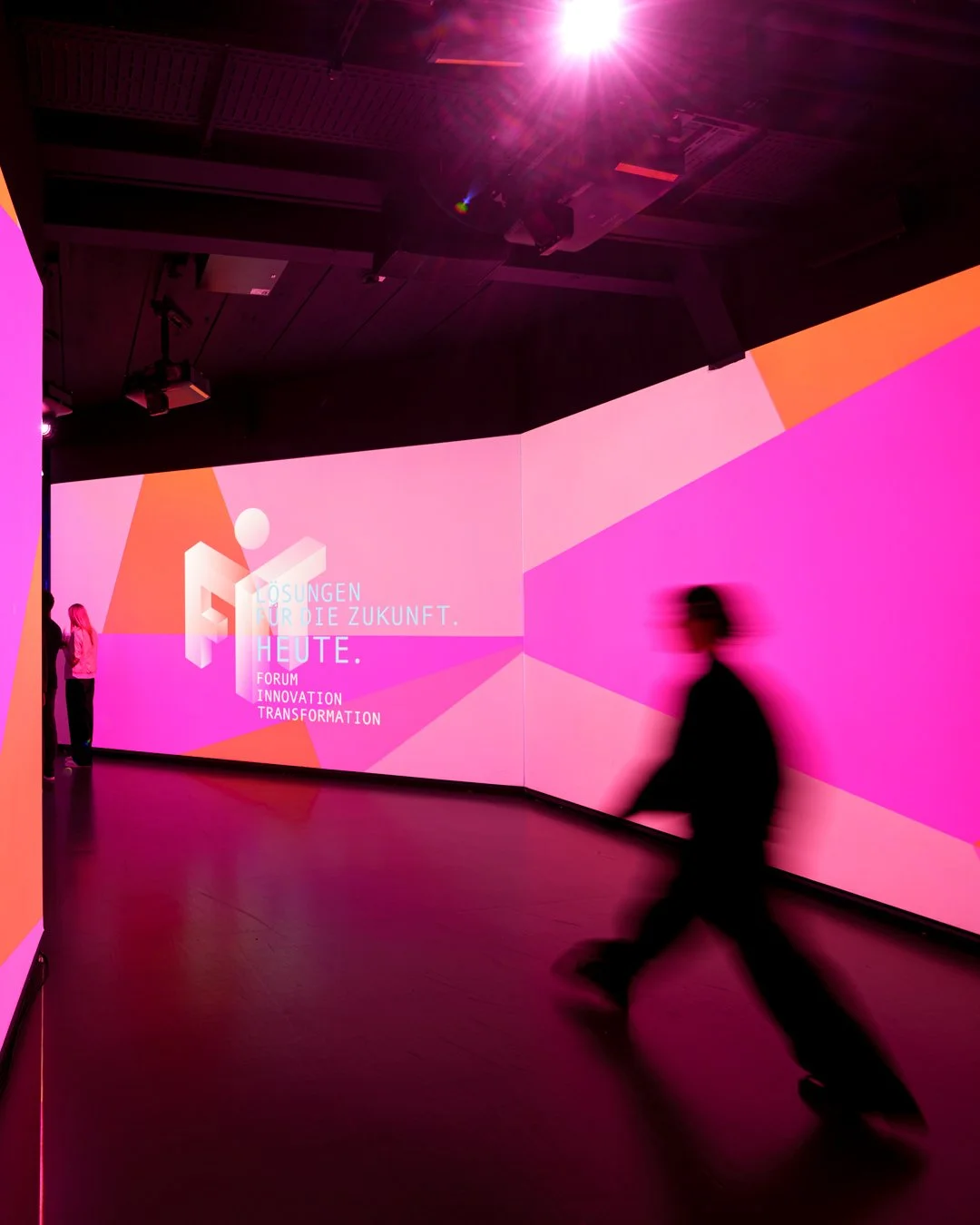 Visitor in front of a large pink projection wall reading FORUM INNOVATION TRANSFORMATION at the FIT event for Kreissparkasse Miesbach-Tegernsee