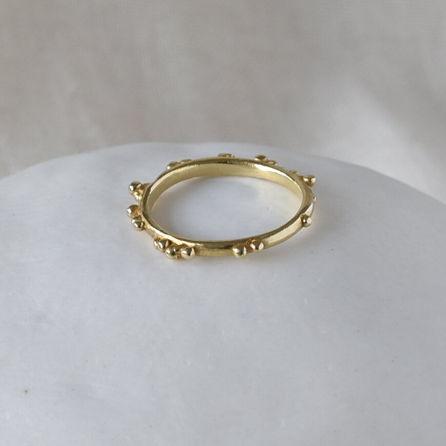 Gold skinny ring with bubble dot texture, slim, delicate shown on white ceramic pebble. Militza Ortiz Jewellery
