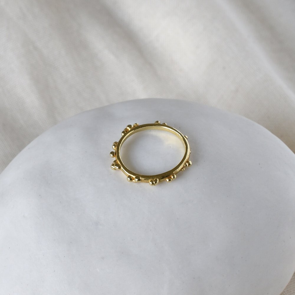 View from top Gold skinny ring with bubble dot texture, slim, delicate on white ceramic pebble. Militza Ortiz Jewellery