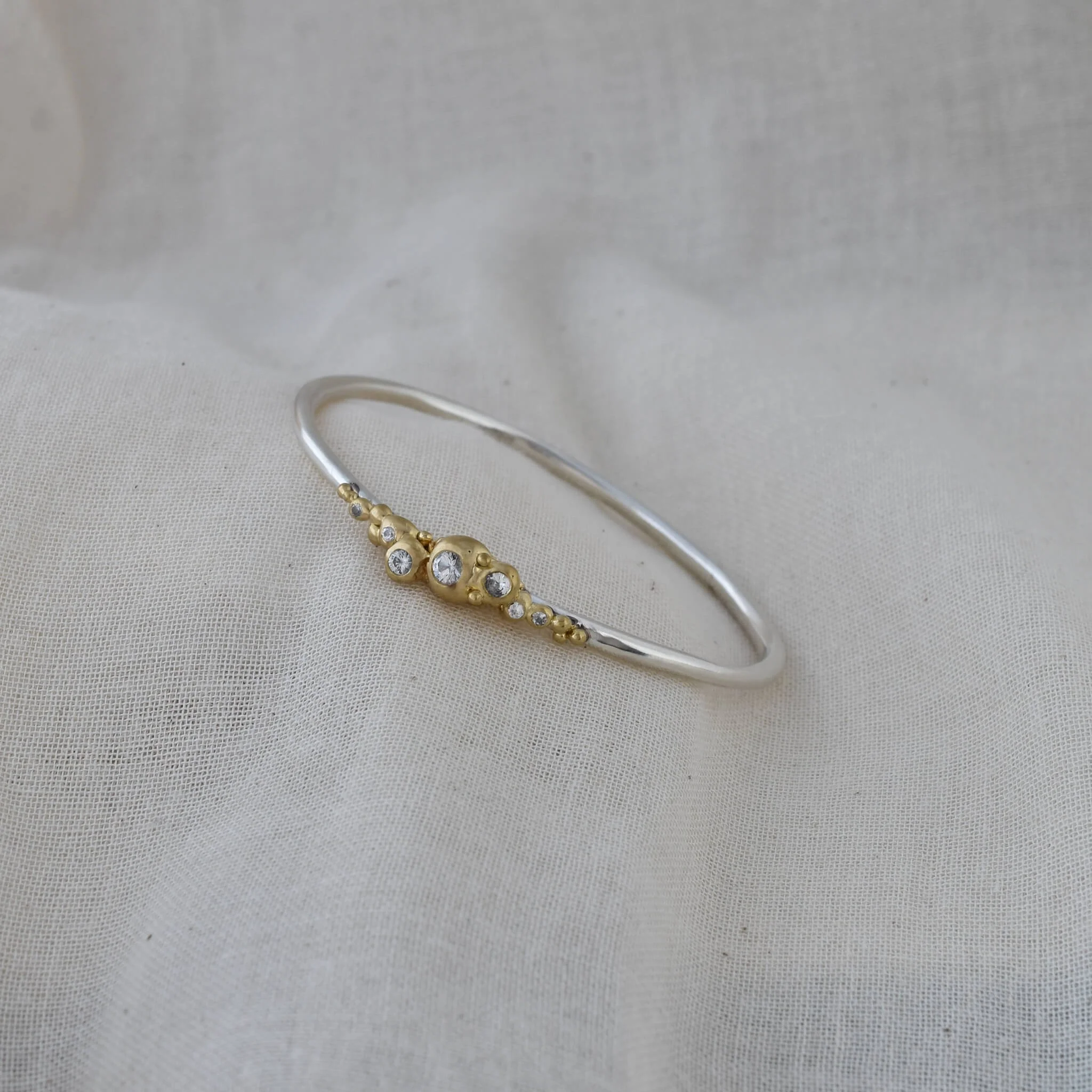 Bangle bracelet in gold and silver with white sapphires set in gold bubbles on white material