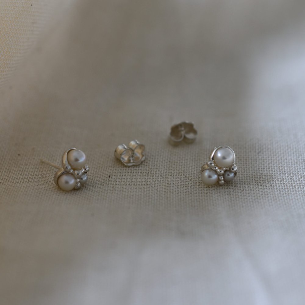 Silver pearl stud earrings shown on linen.  Three different sized white pearls with silver granules