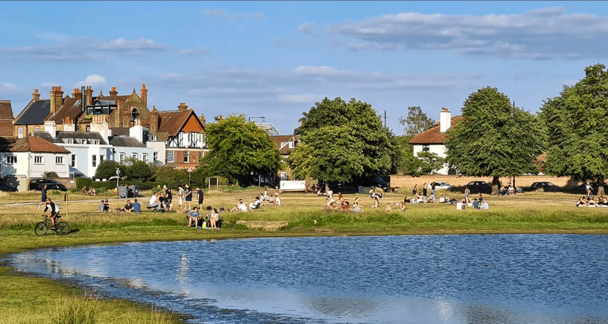 People gathered around pond in Wimbledon common.
