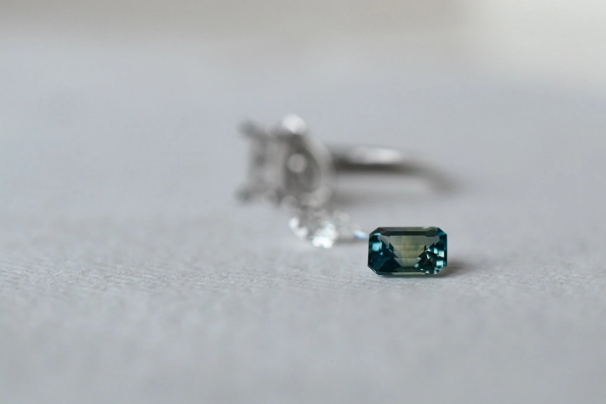 Bi coloured blue and green octagon sapphire with diamond and platinum ring in the background