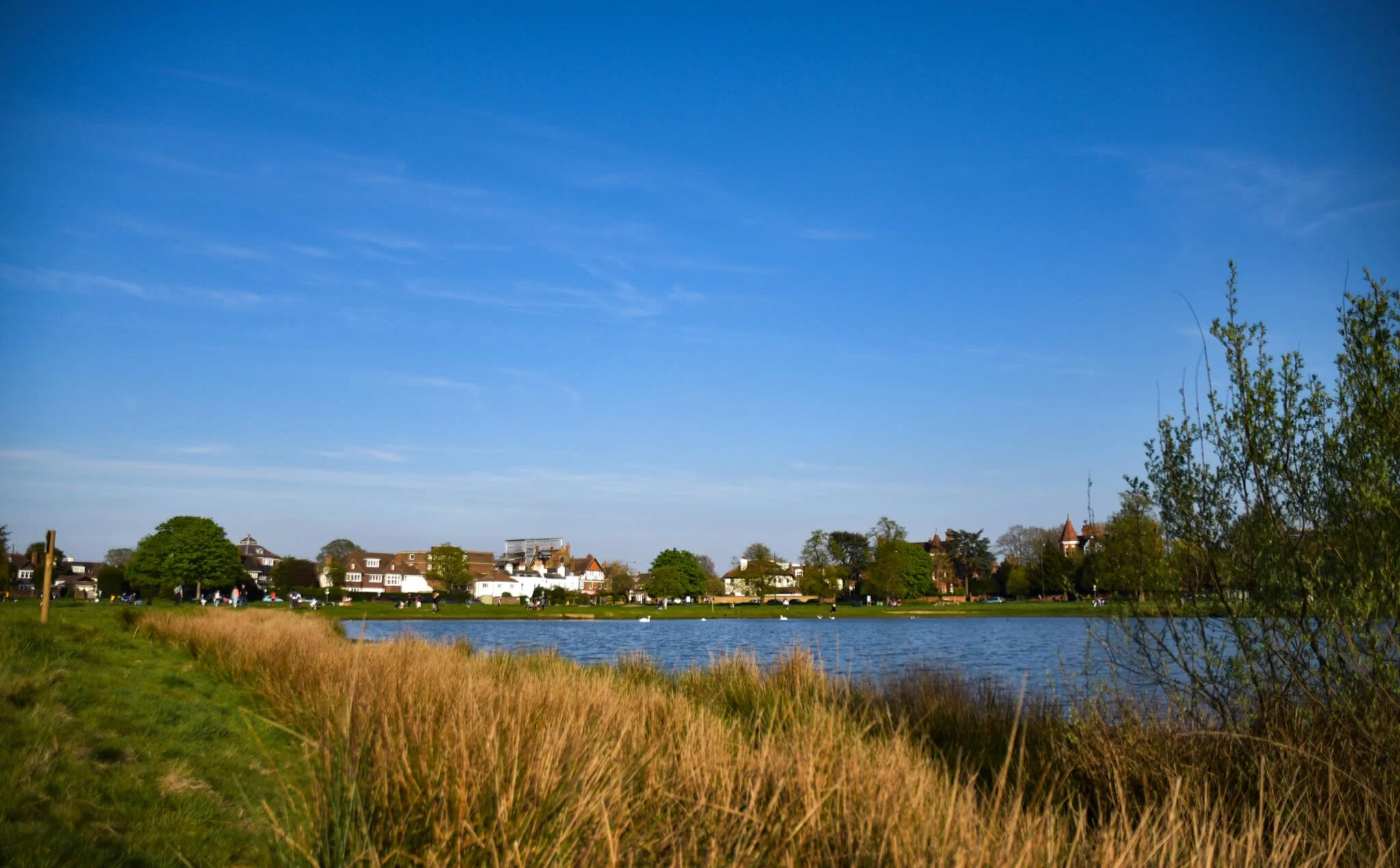 Pond with English houses in background and blue skies.