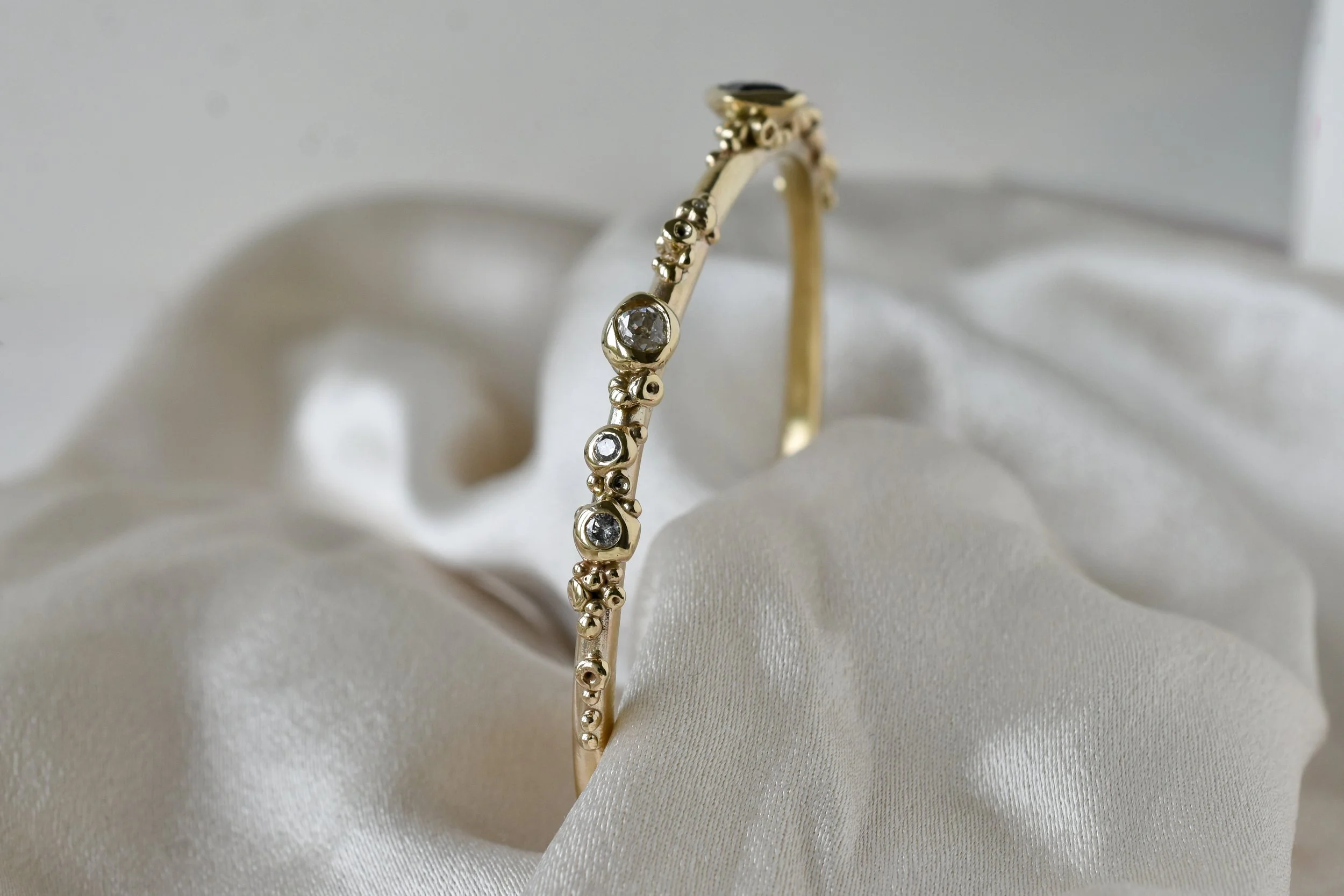Gold bangle with Salt and pepper diamonds encrusted like coral reef made by Militza Ortiz shown on silk