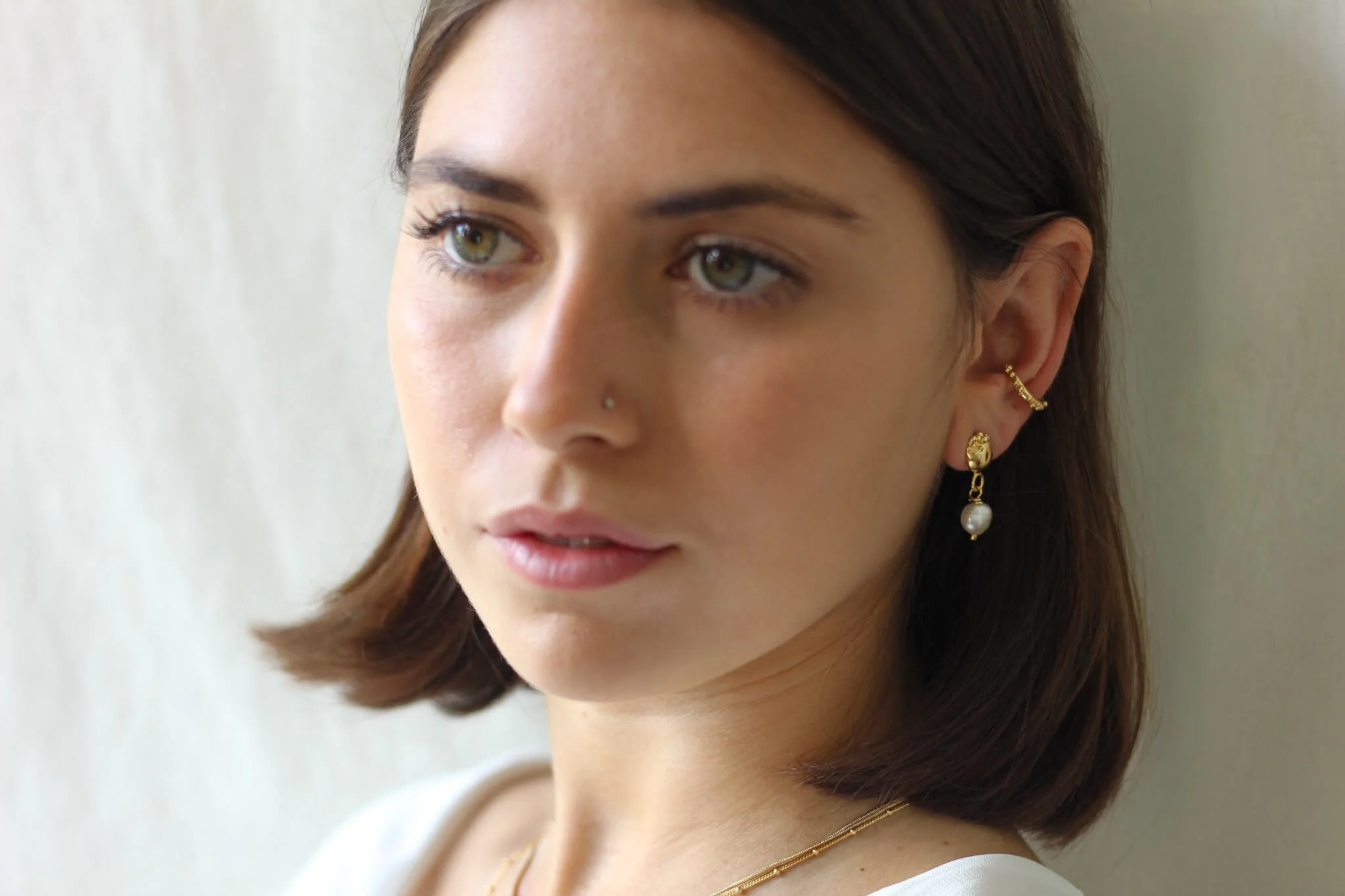 Brunette model wearing pearl earrings and gold ear cuff