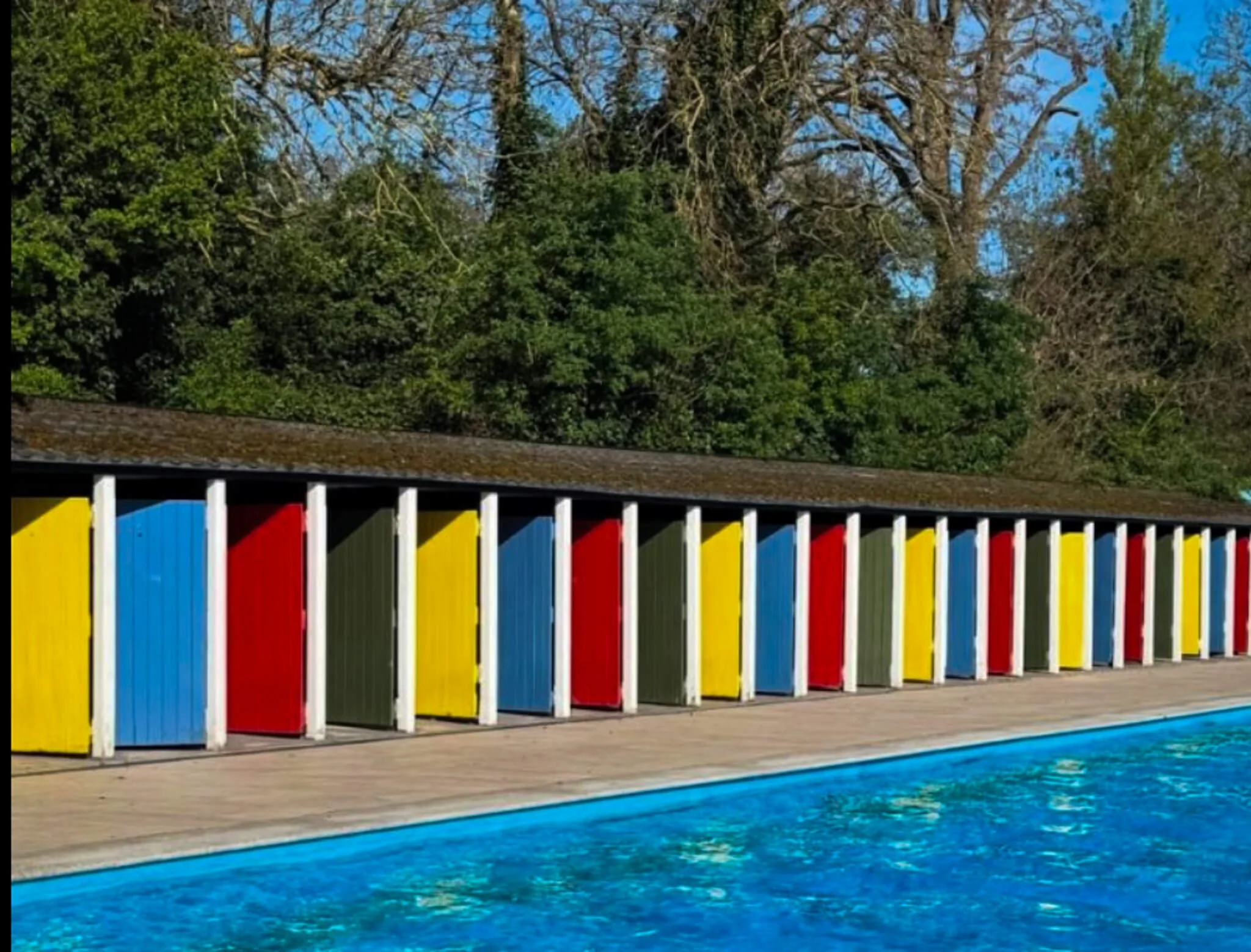 Yellow, blue, red and green changing rooms with pool in front.