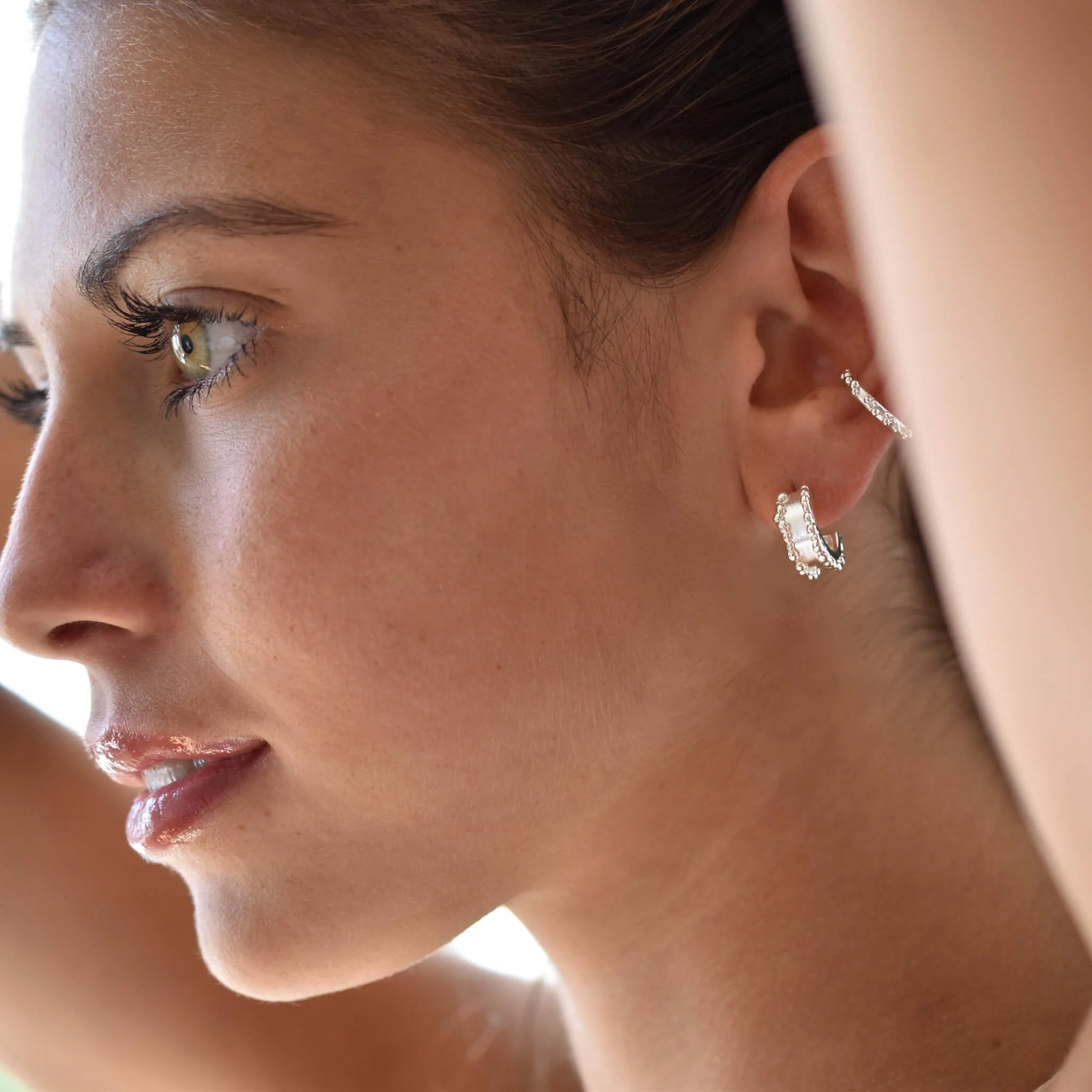 Close-up of a woman's face showing her eye, cheek, and ear with multiple earrings.