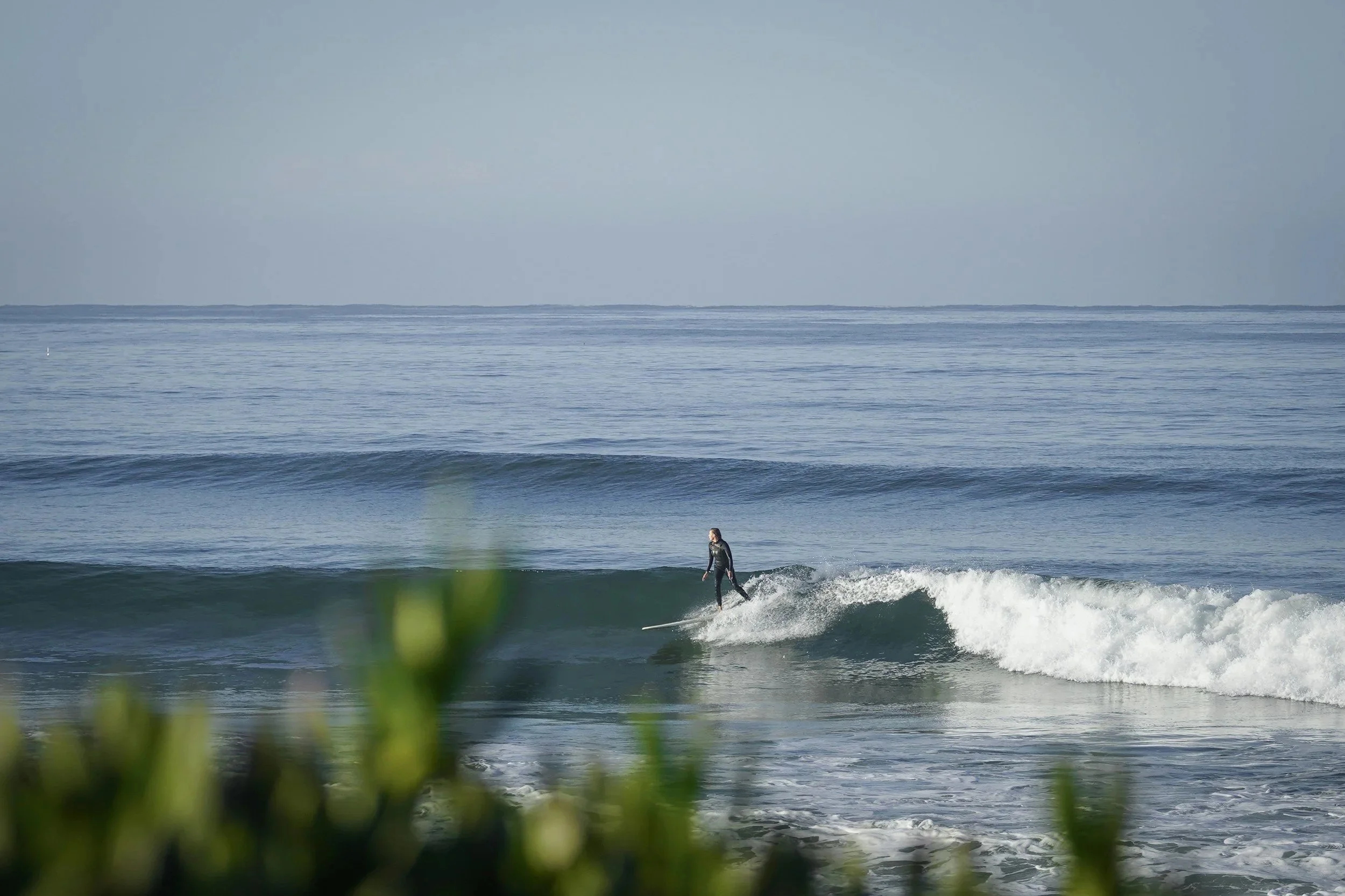 Ein Surfer, der auf einer Welle reitet, vor dem Meer und einem Himmel mit einigen Wolken.