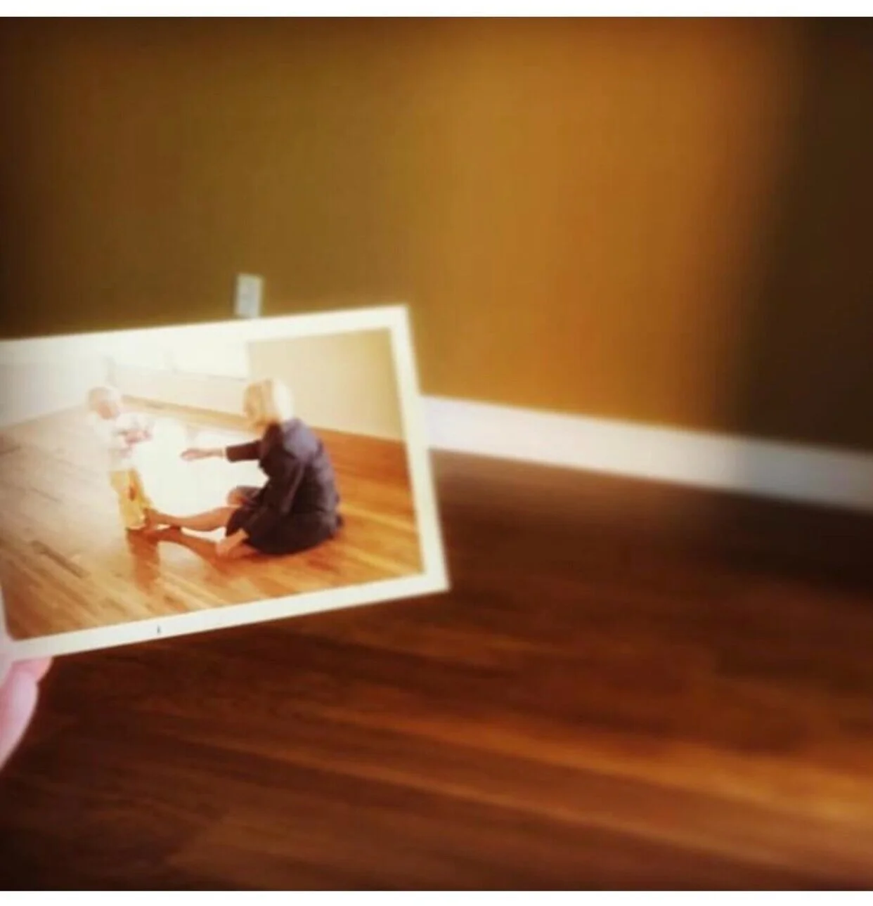 A person holding a photograph of two people sitting on a hardwood floor, one is a baby and the other is a mother