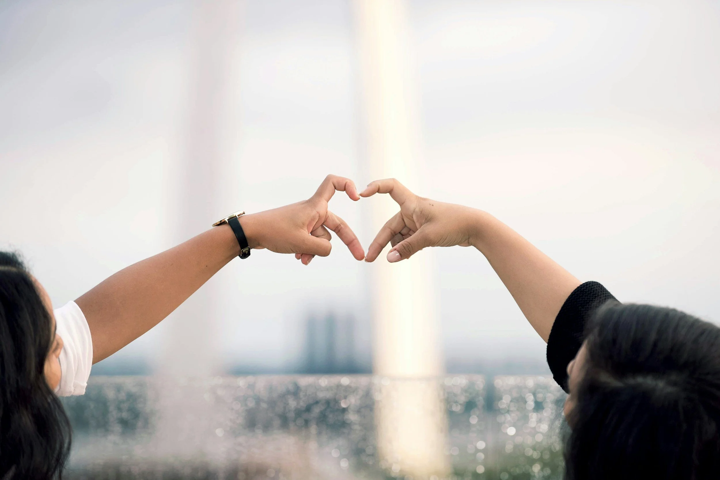 Two people reach out, making the shape of a heart with their connected hands.