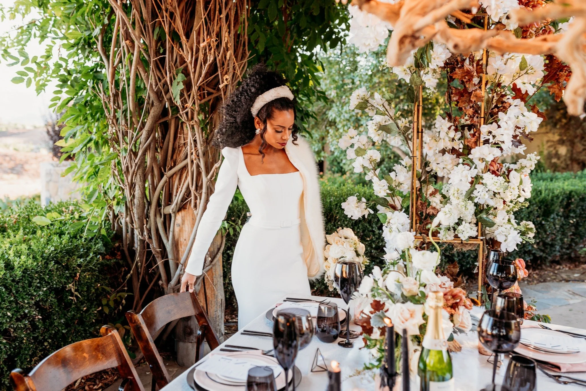Bride posing beside reception table at South Coast Winery vineyard wedding editorial with floral arrangements and candlelight