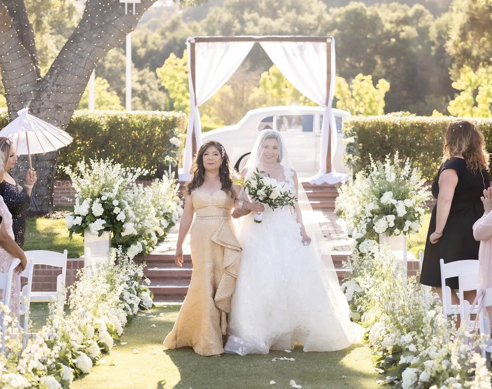 Bride walking down ceremony aisle at Sherwood Country Club with lush white floral aisle design