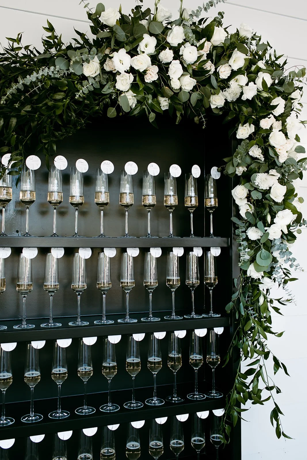 Champagne escort card display with champagne flutes and lush greenery floral installation at estate wedding