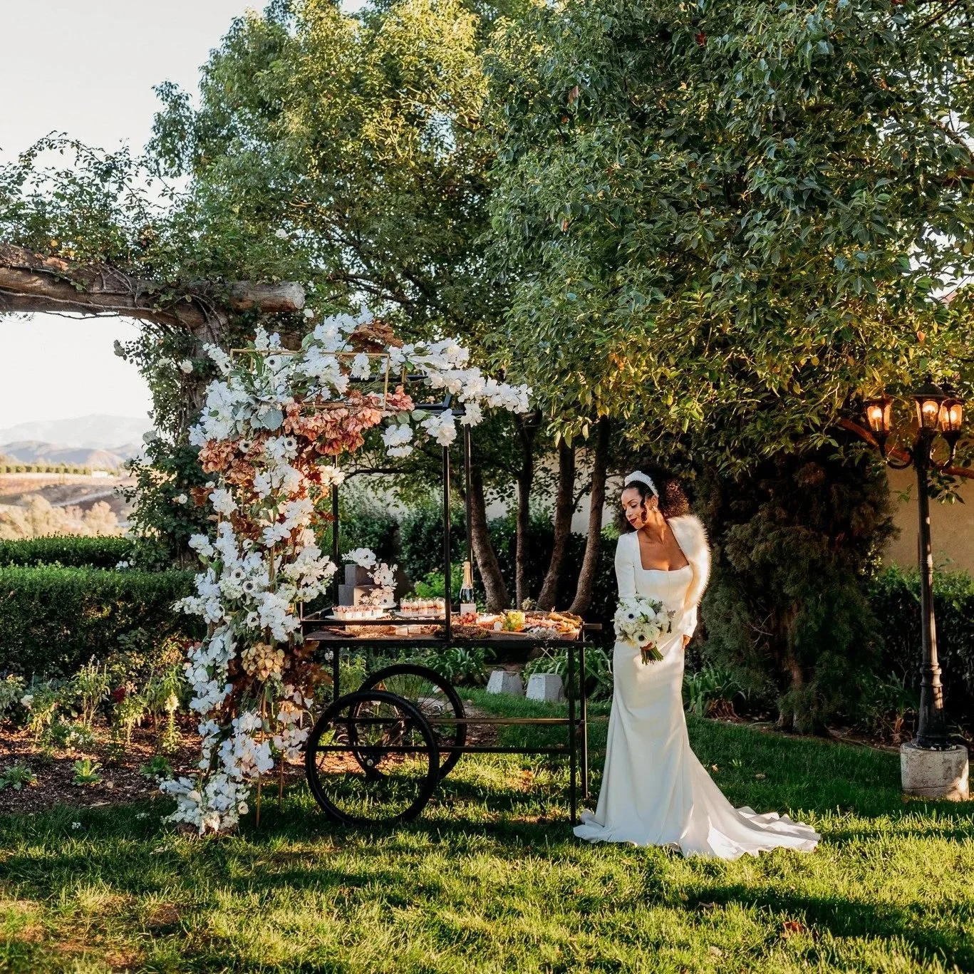 Bride standing next to a dessert cart with cascading florals and layered textures at South Coast Winery fall vineyard wedding editorial