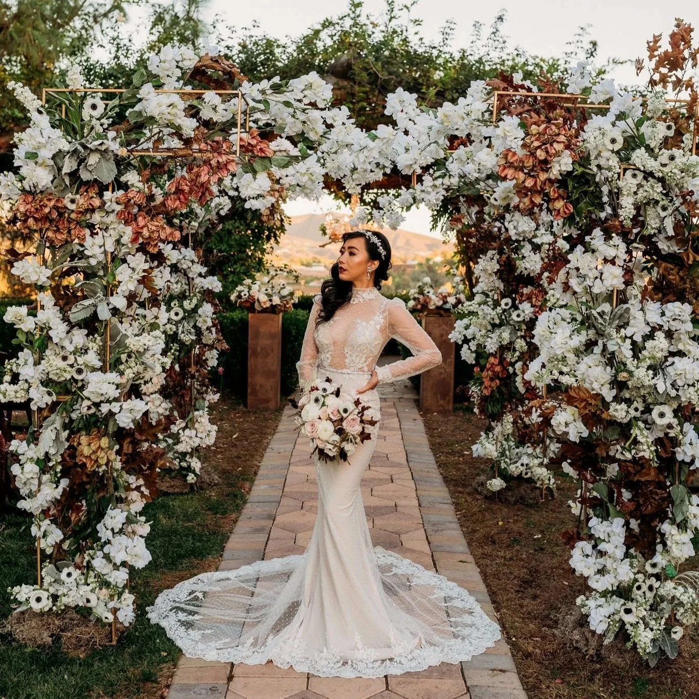 Bride standing beneath floral ceremony arch at South Coast Winery fall wedding editorial in Temecula with white and autumn-toned florals